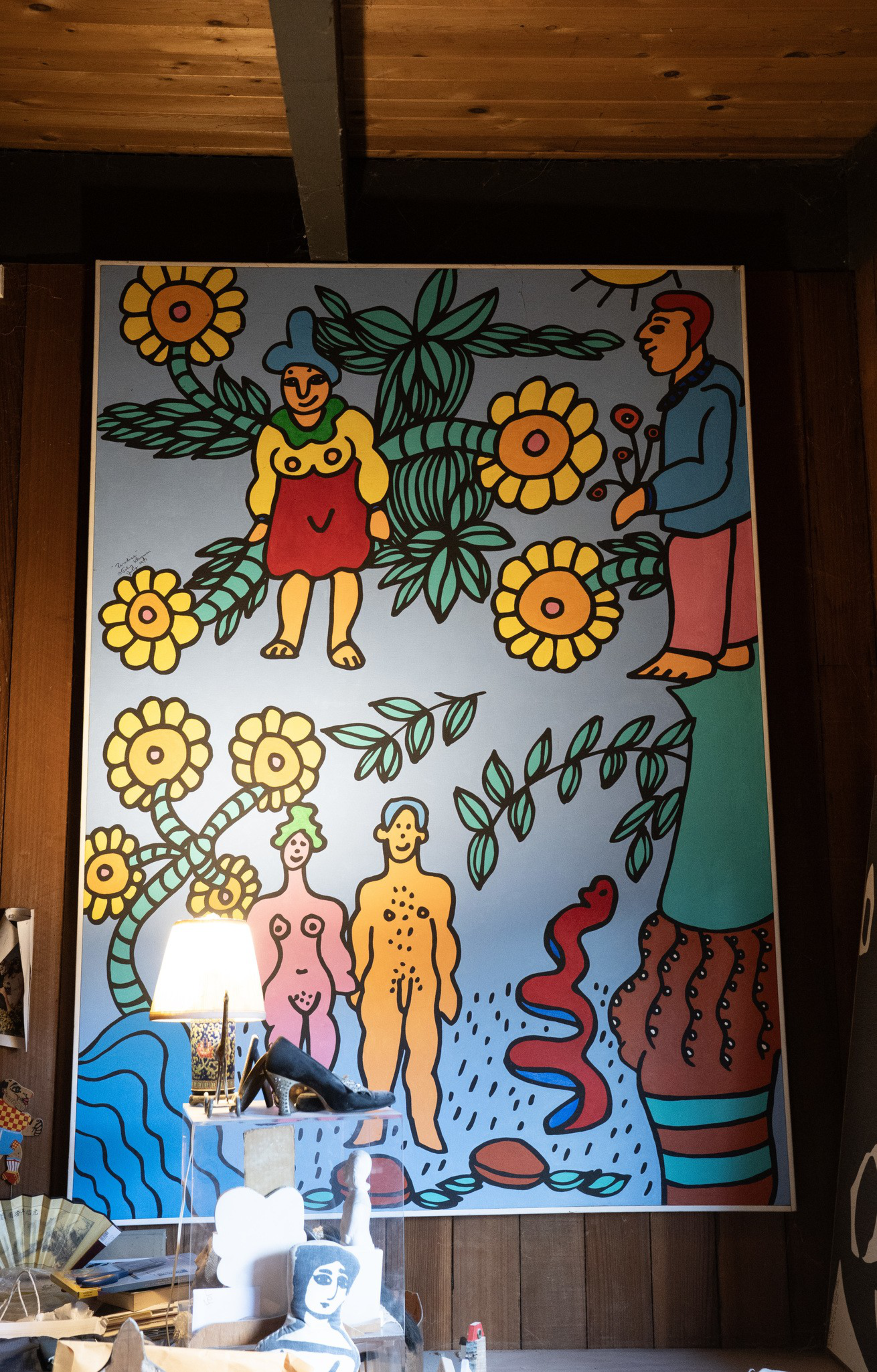 Bold, colorful painting features stylized human figures, large flowers, green leaves, and abstract patterns set against a blue background.