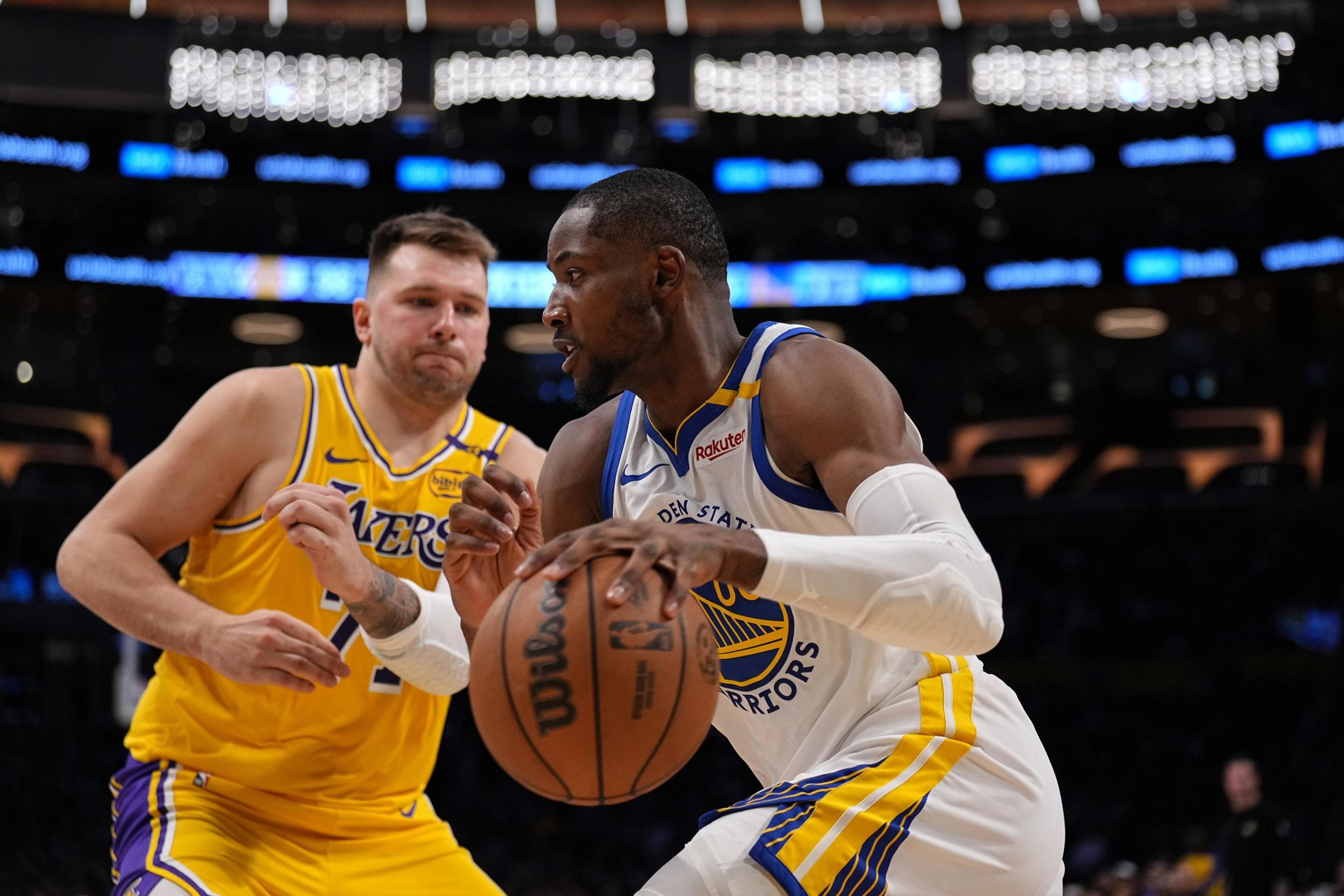 Two basketball players are in action. One in a yellow jersey defends, while the other in a white jersey dribbles the ball, both focused amidst a lively arena.