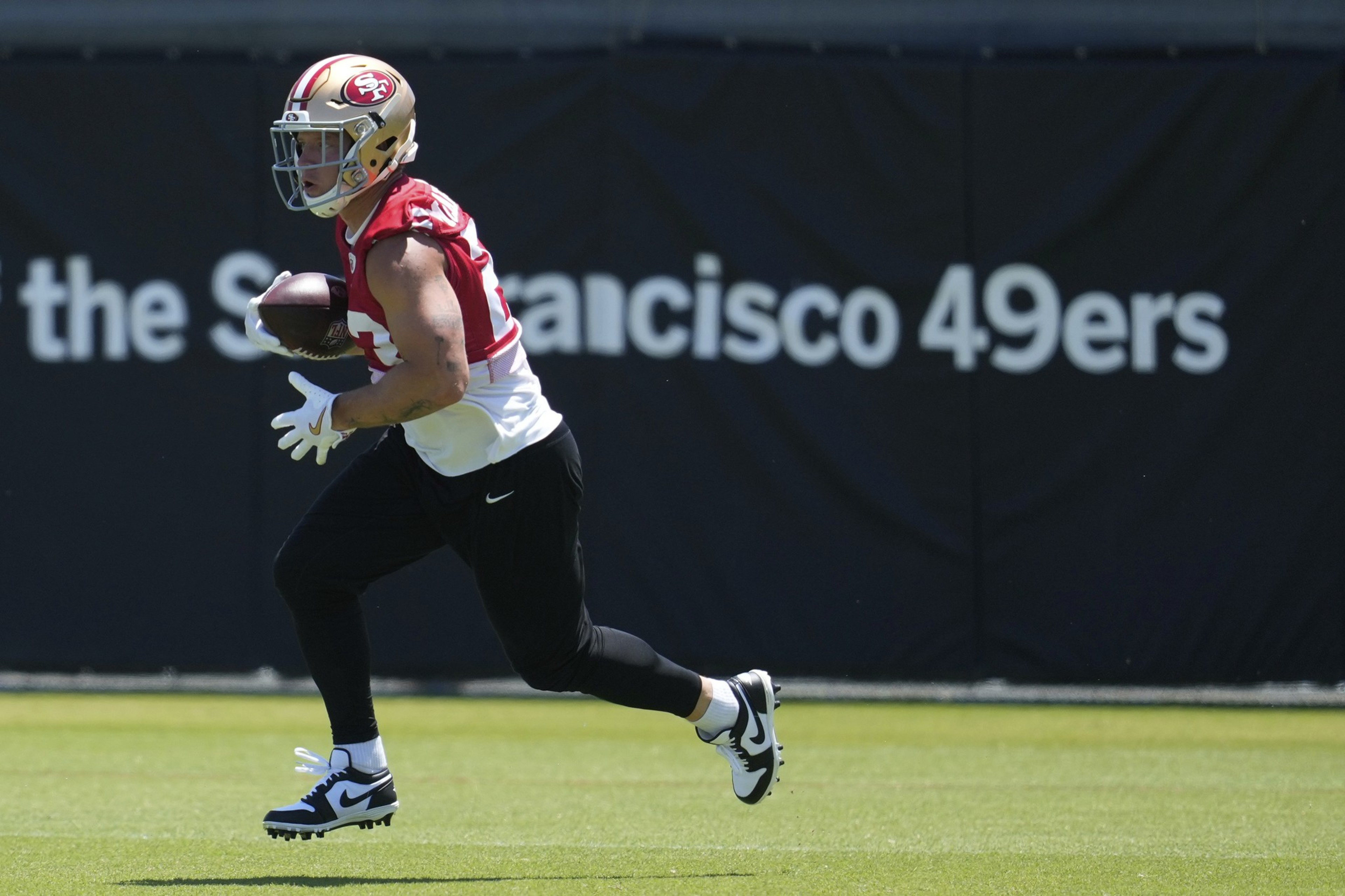 A football player in a 49ers jersey runs on a field, holding a football. A black background displays "San Francisco 49ers" in white text.