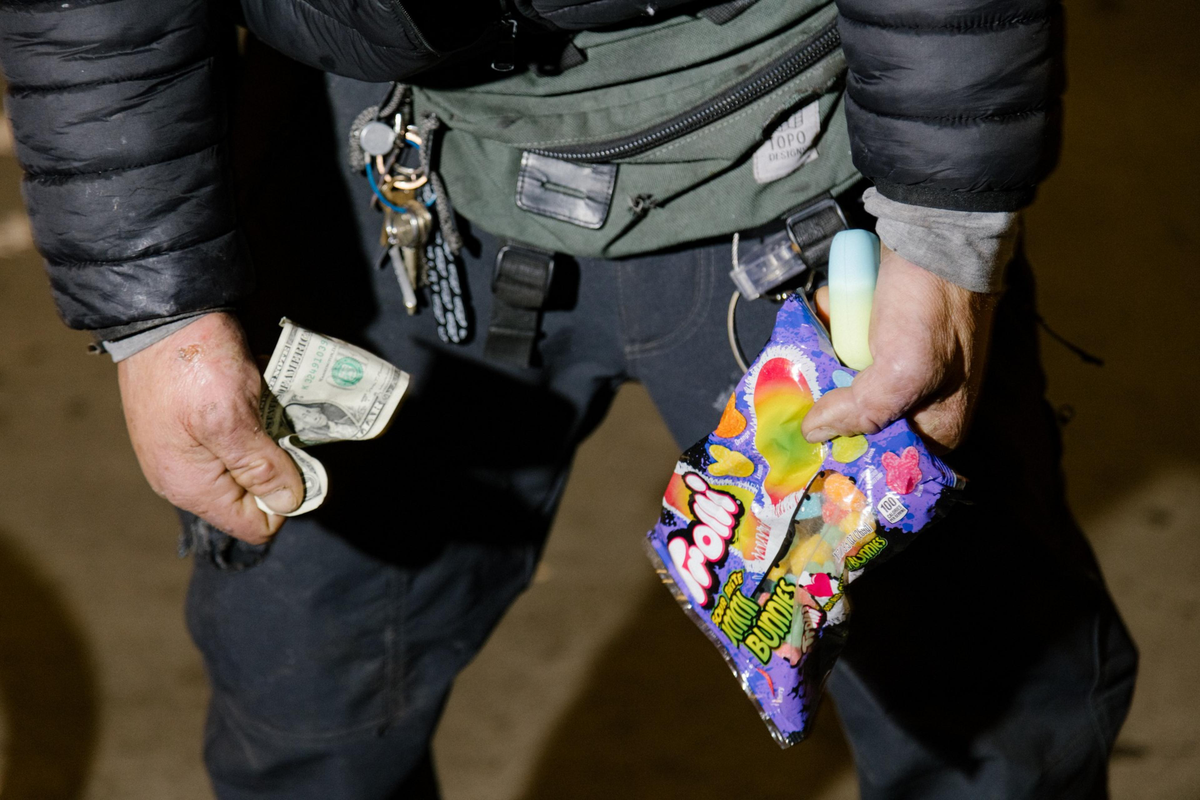 A man holds money, and candy for sale in his hands.