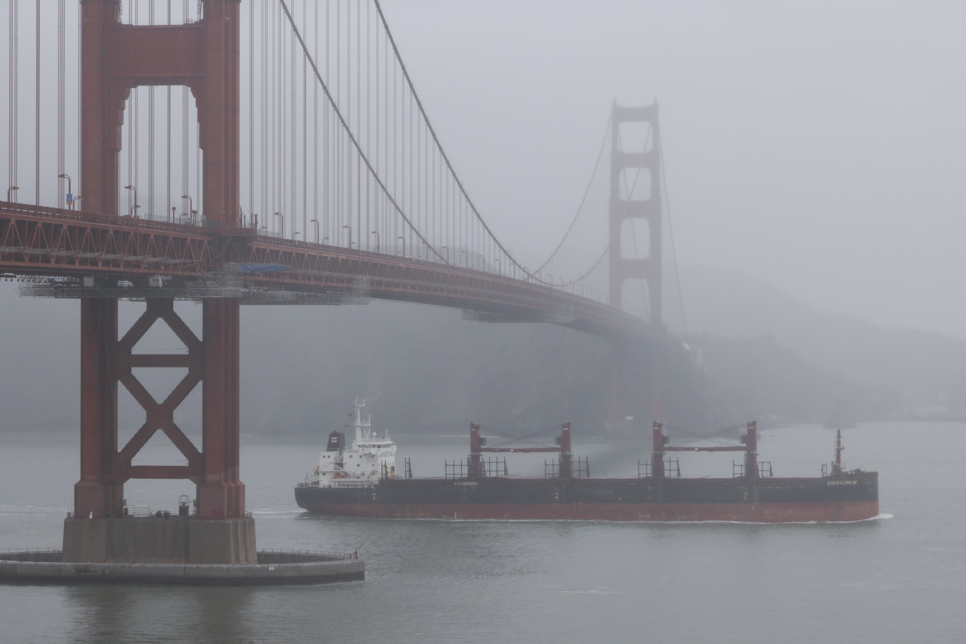 A ship passes under a bridge in rainy weather.