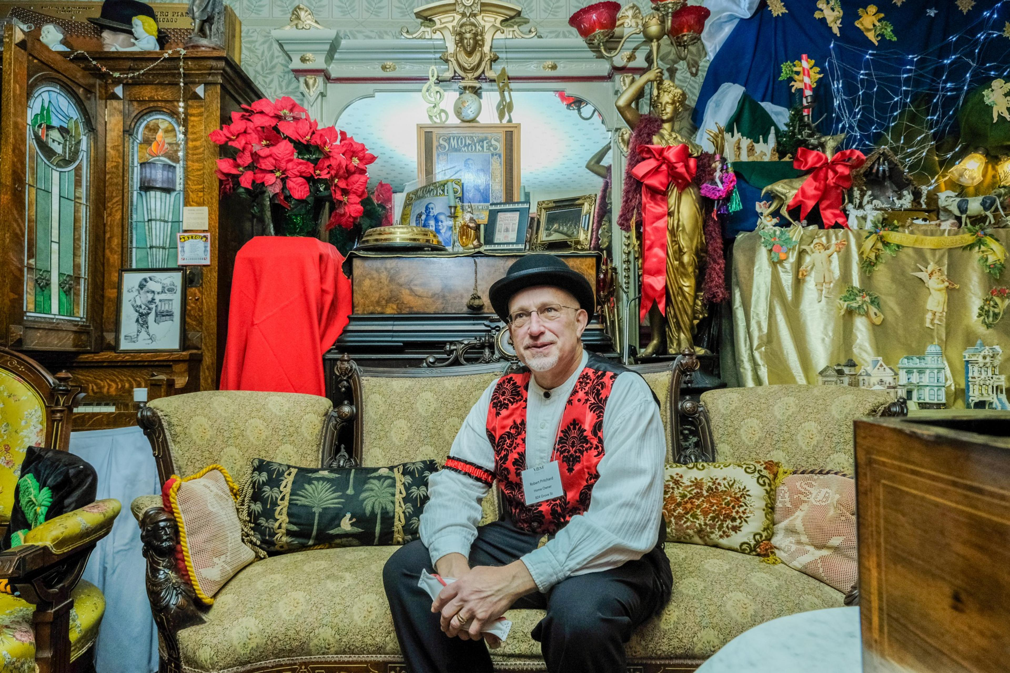 A person sits on a couch with a red vest and white dress shirt.