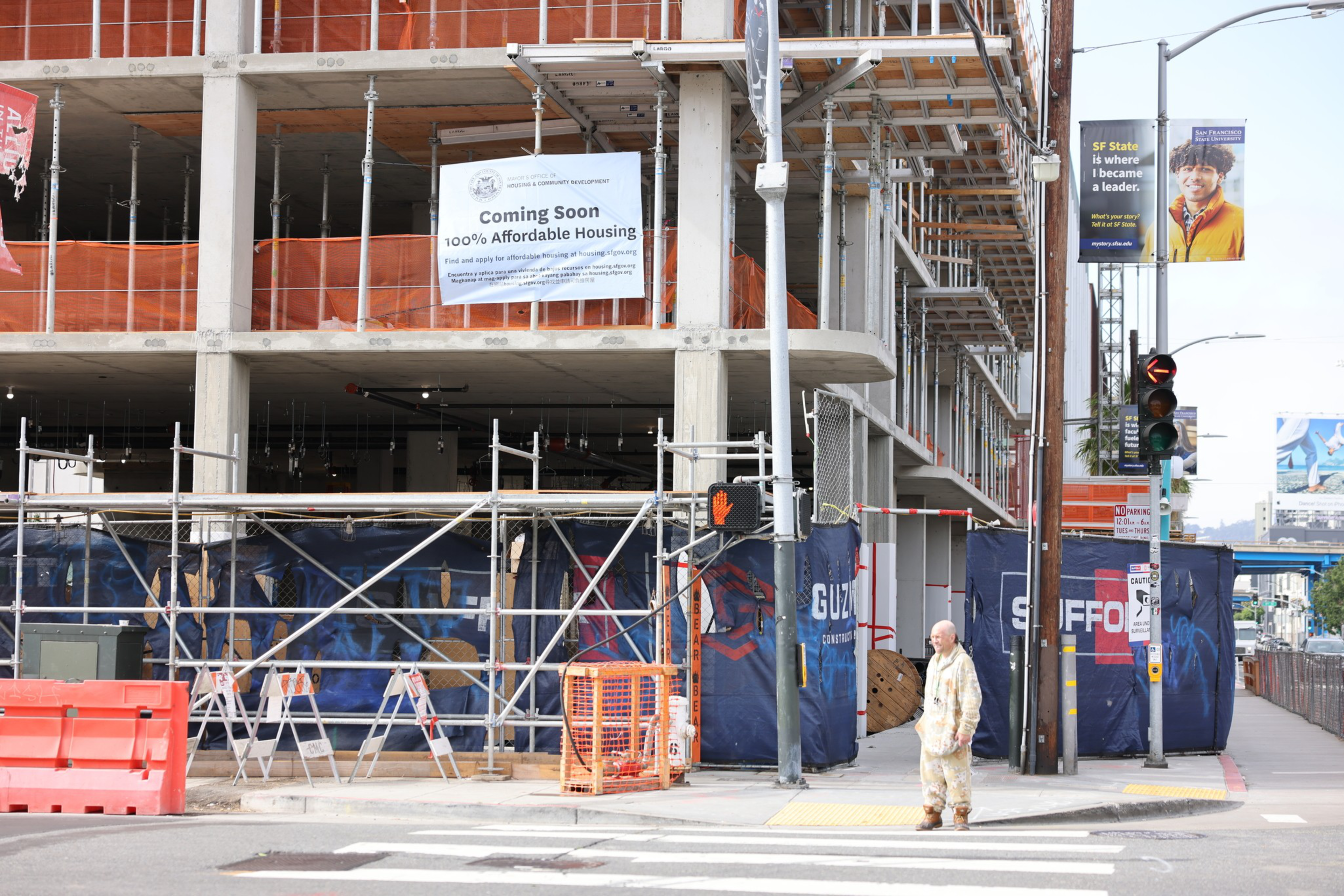 Pedestrian stands under scaffolding and unfinished beams of a building under construction.