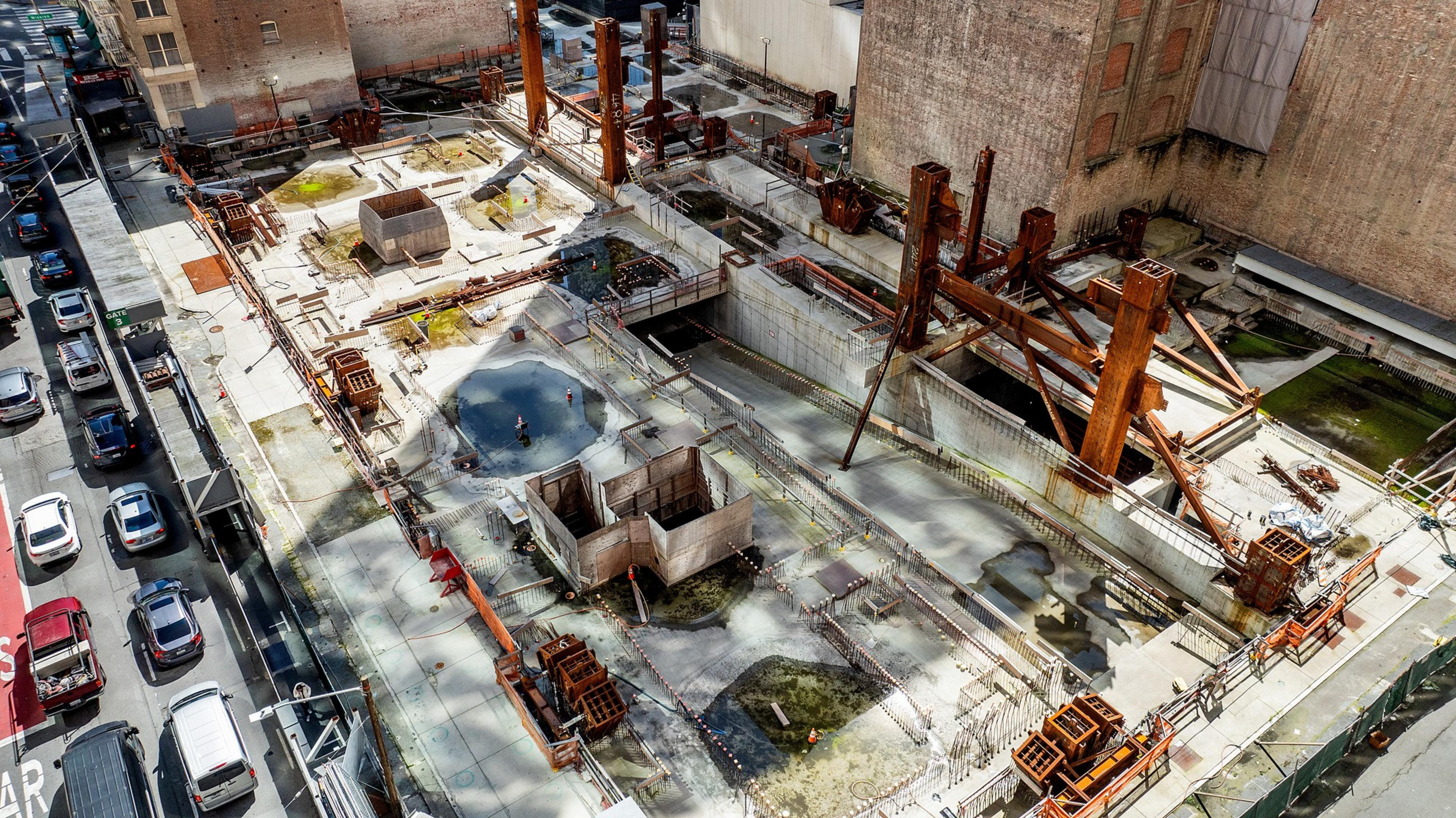 Aerial view of an urban construction site with exposed steel frameworks and adjacent traffic.