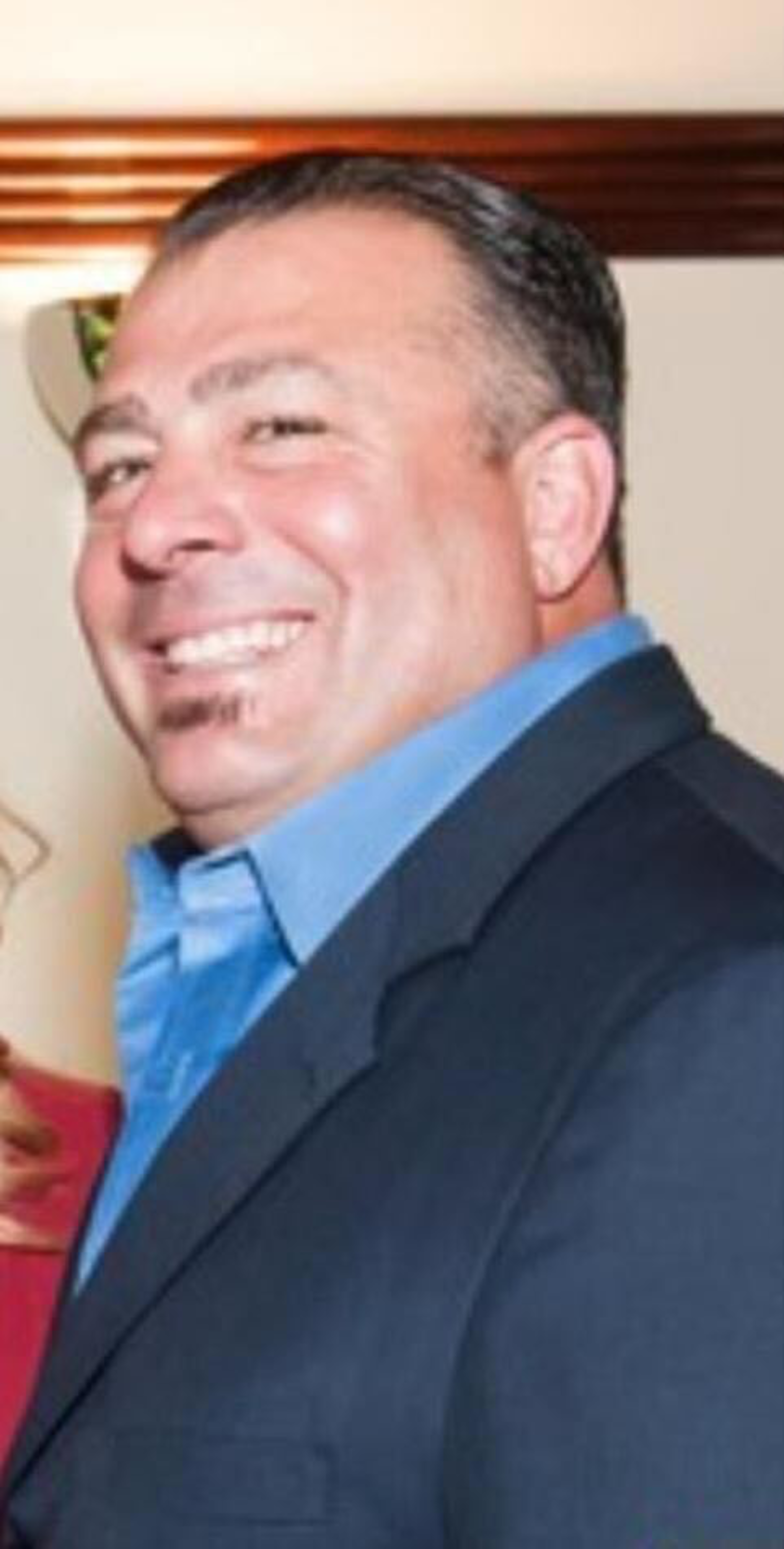 A smiling man in a suit with a blue tie, captured from the side.