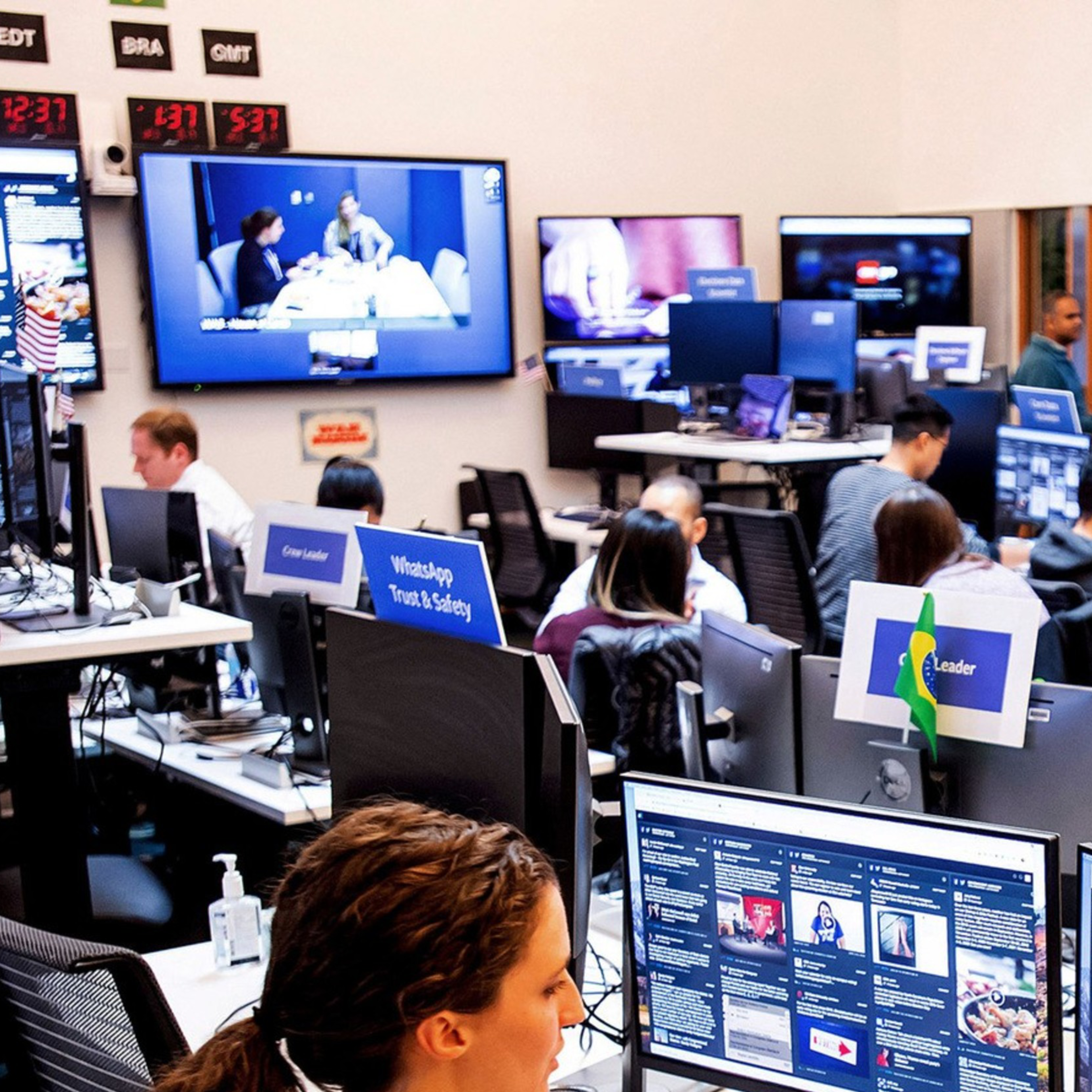People work at a busy control center with numerous monitors, displaying various digital interfaces and video feeds, under labeled sections like "Operations."