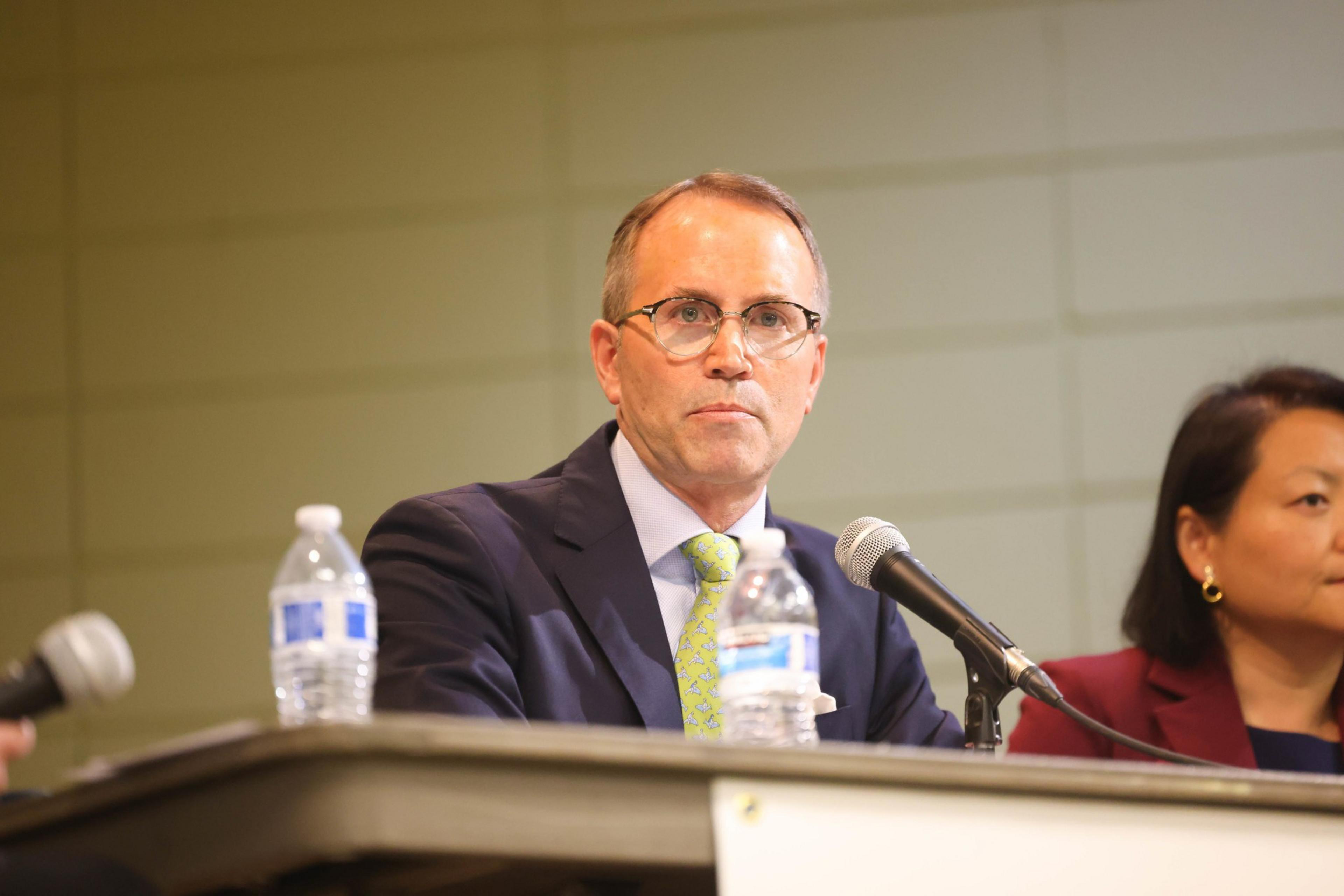 A man in a suit speaks into a mic.