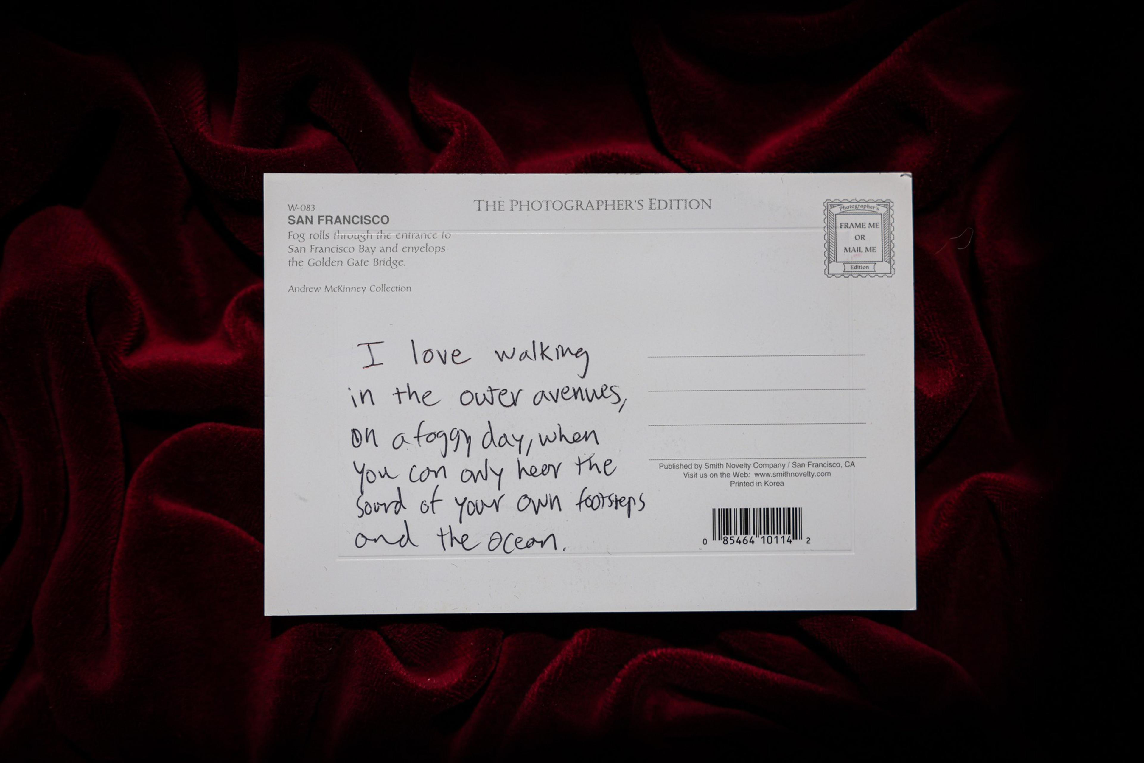 A postcard with handwritten text about loving foggy walks on outer avenues, placed on dark red velvet fabric.