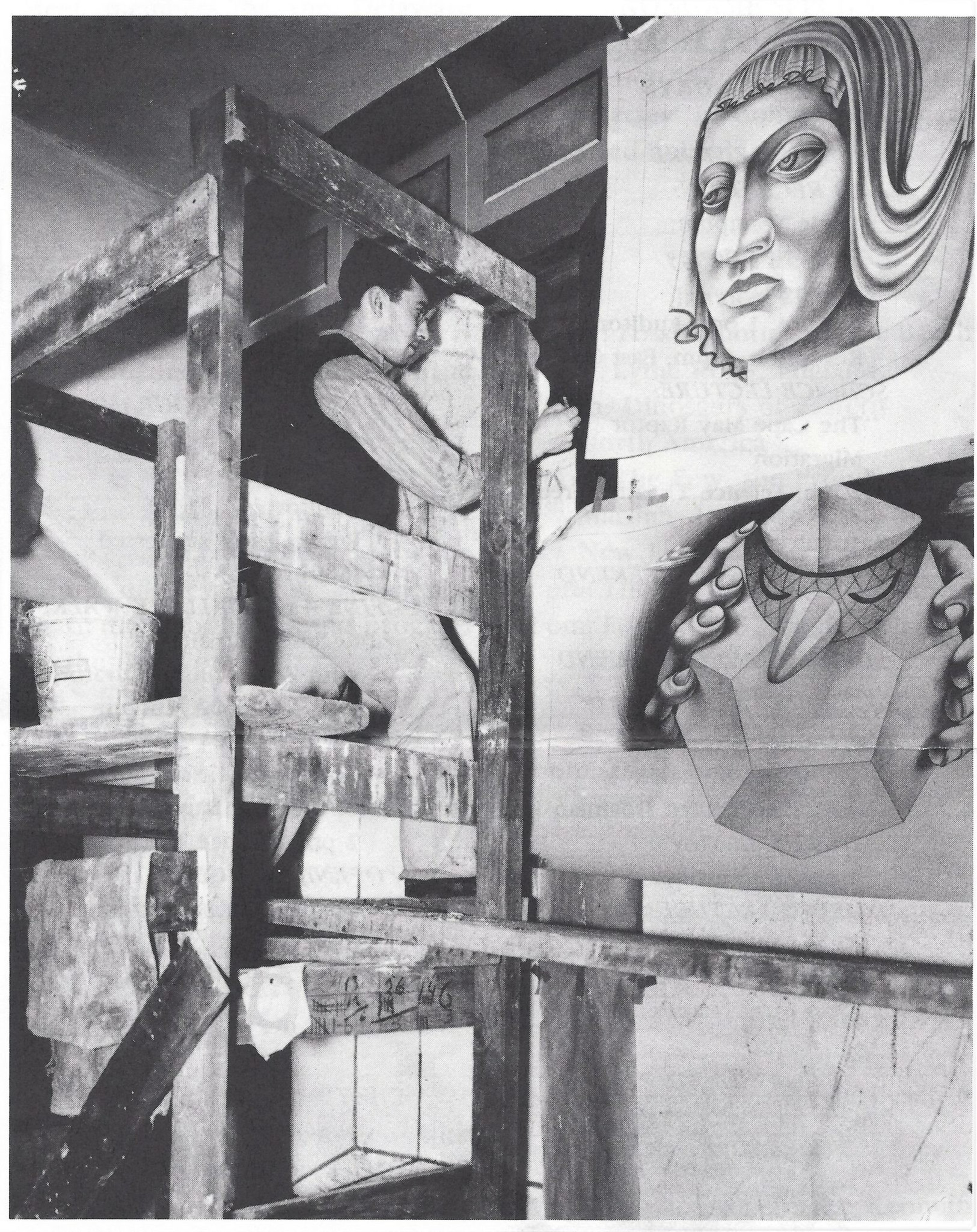 A man stands on a wooden scaffold, working on a large mural featuring a stylized face and geometric shapes with hands around them.