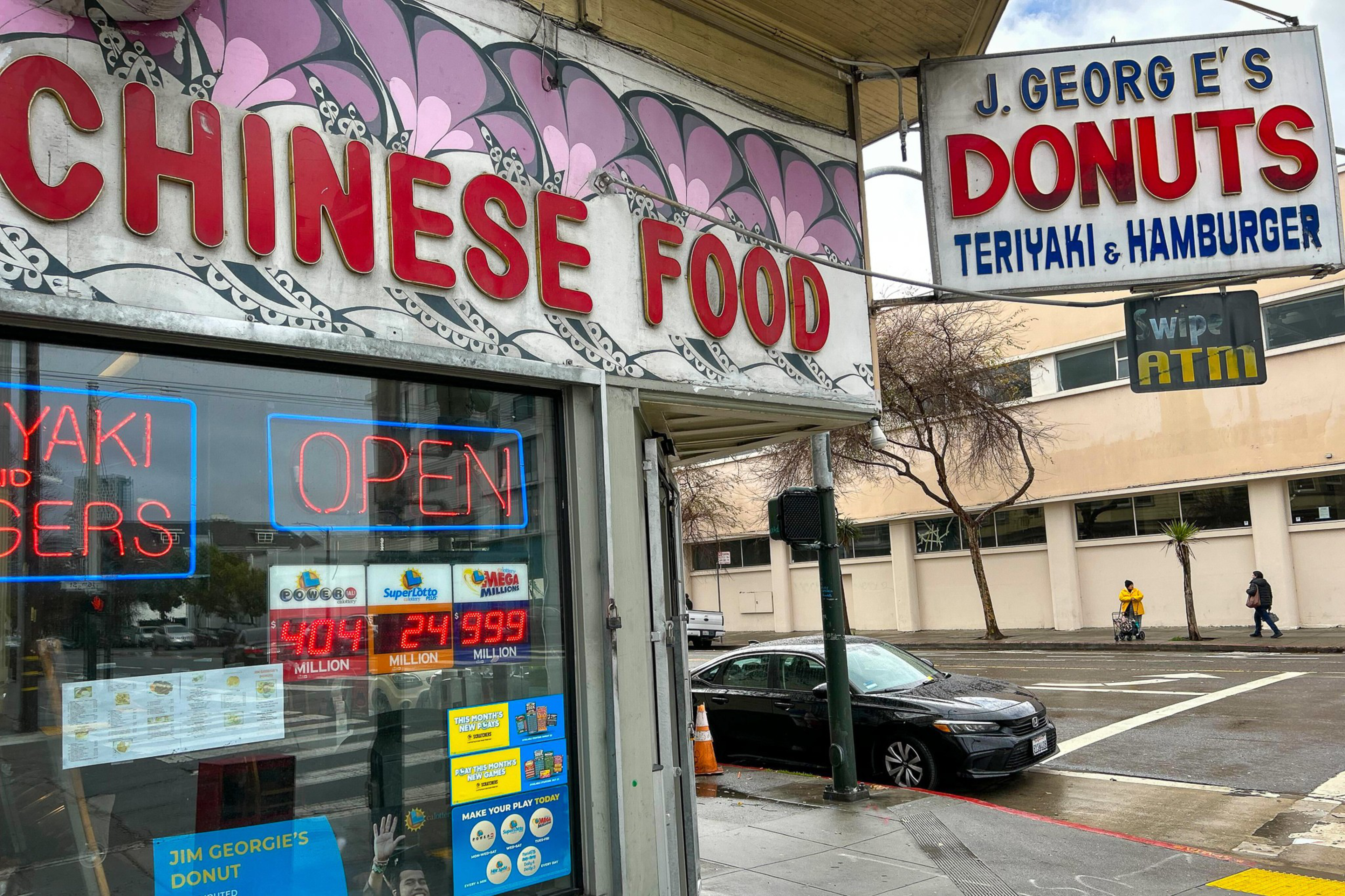 A storefront displays large "CHINESE FOOD" letters, neon "OPEN" sign, and lottery posters, while a street sign advertises "J. George's Donuts, Teriyaki & Hamburger."