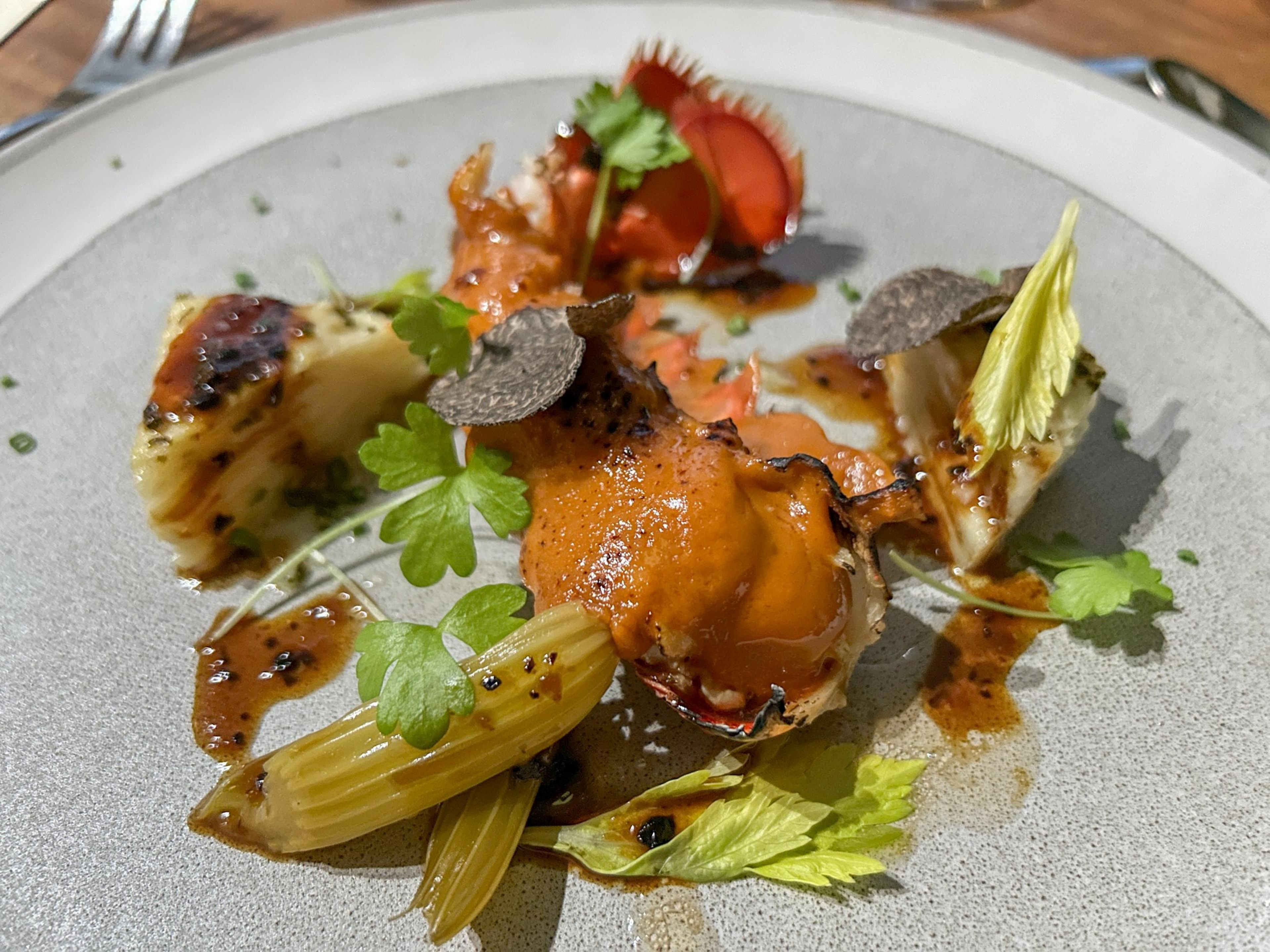 A gourmet dish with lobster, sliced strawberries, greens, and drizzled sauce on a speckled plate.