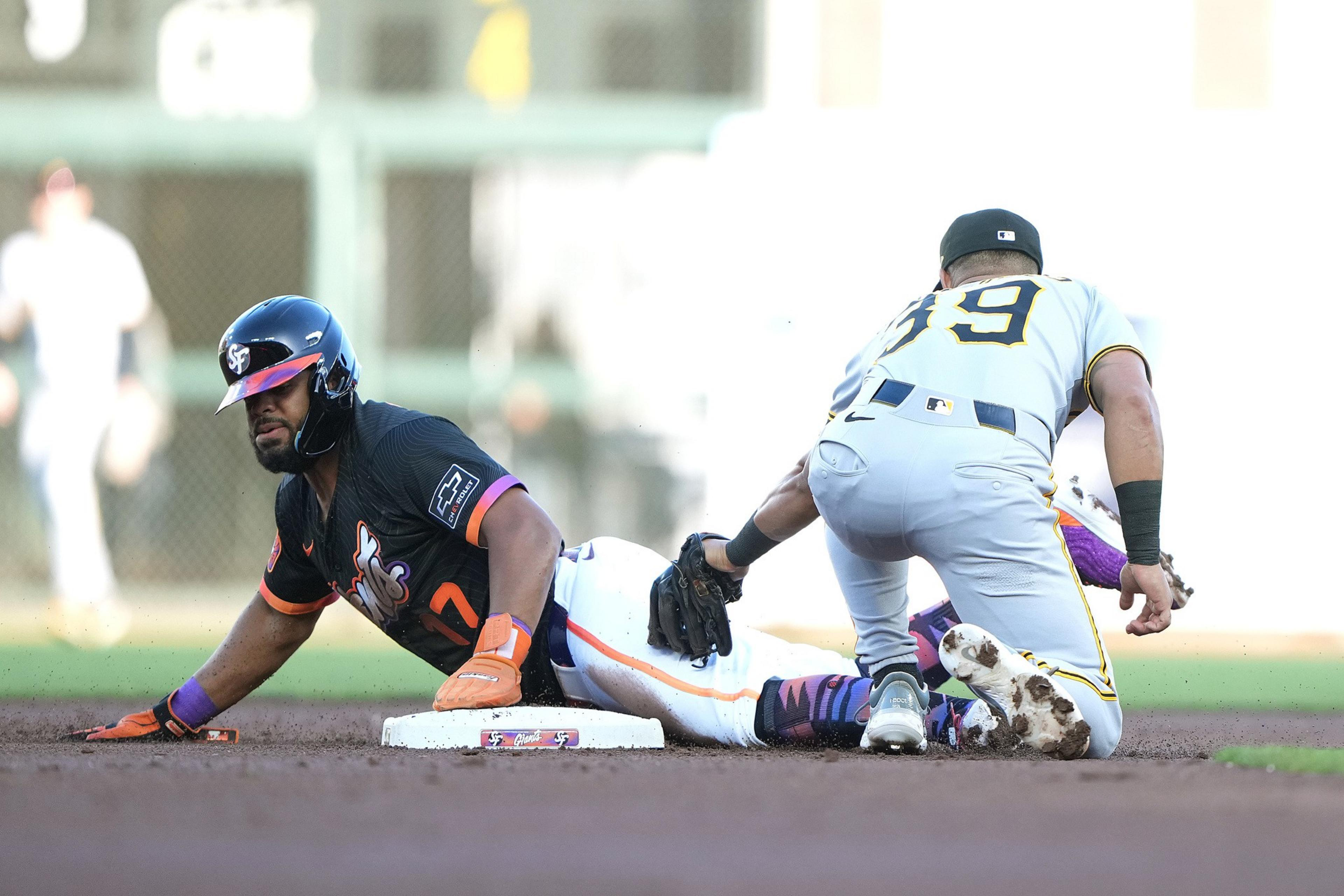 A baseball player in a dark uniform slides headfirst into a base as another player in a gray uniform attempts to tag him out.