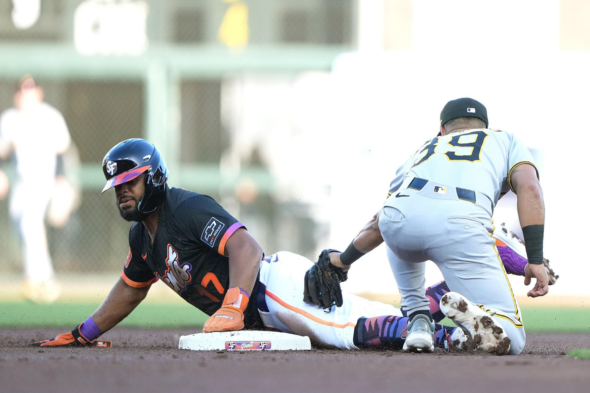 A baseball player in a dark uniform slides headfirst into a base as another player in a gray uniform attempts to tag him out.