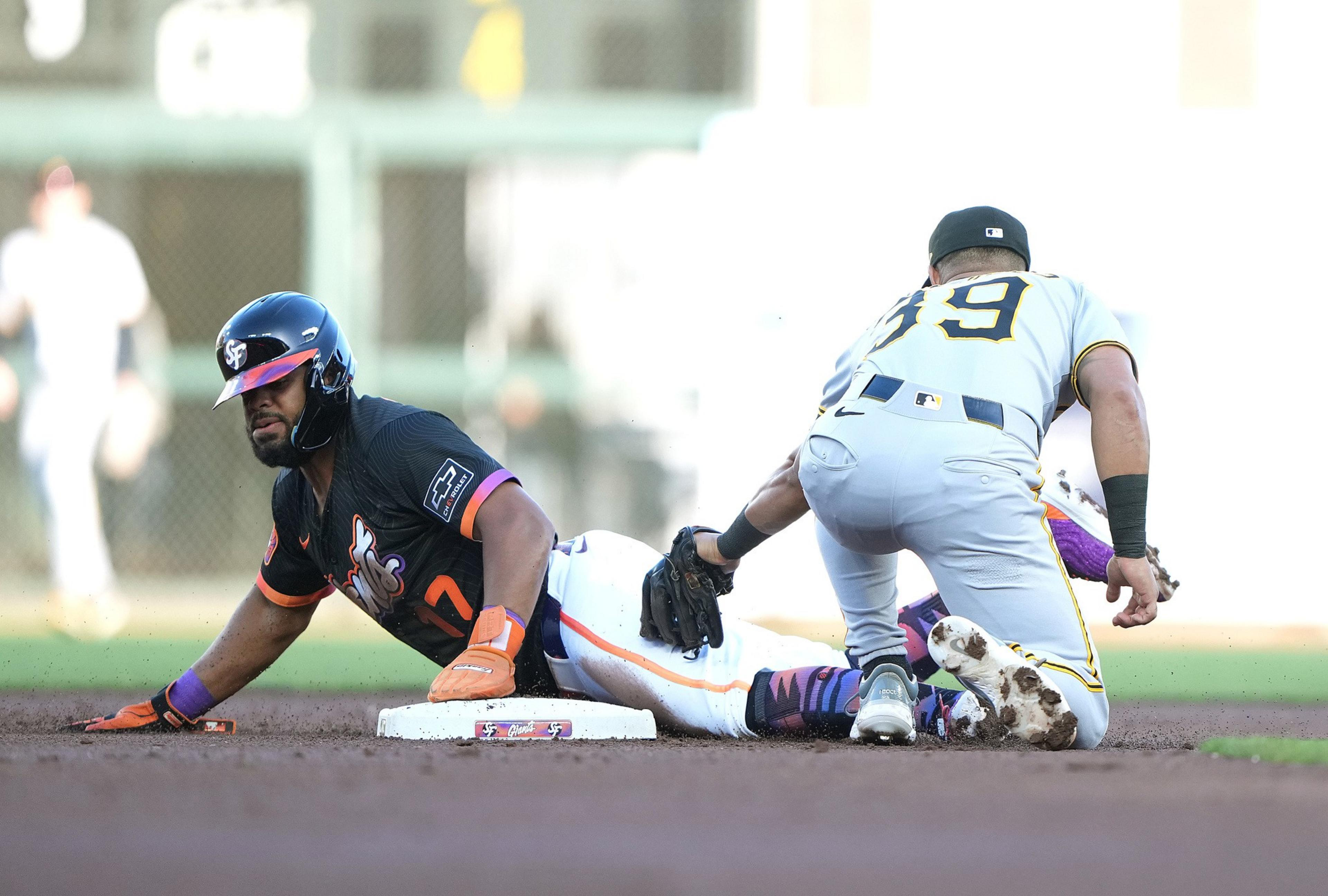 A baseball player in a dark uniform slides headfirst into a base as another player in a gray uniform attempts to tag him out.