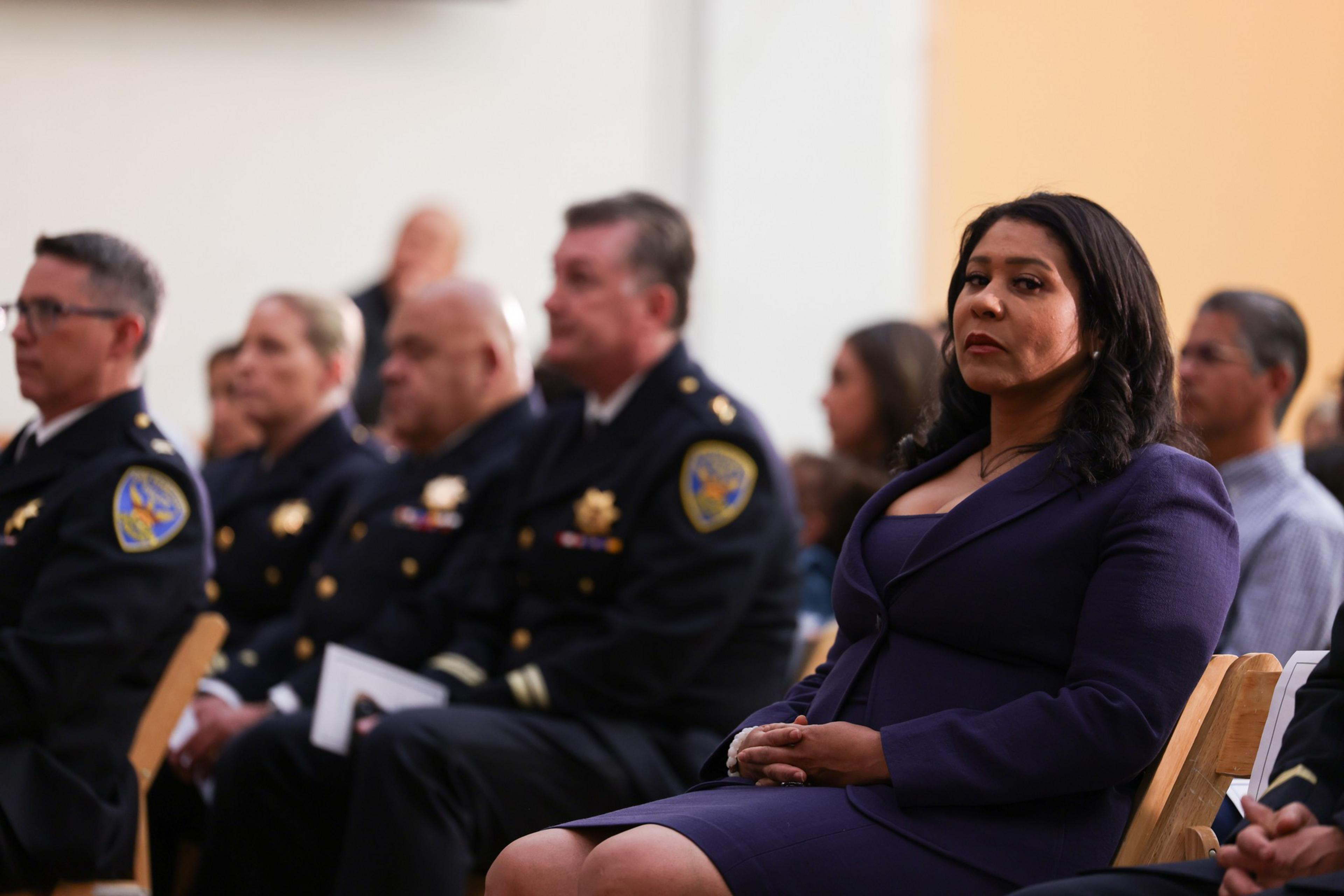 A woman sits next to a row of police officers.