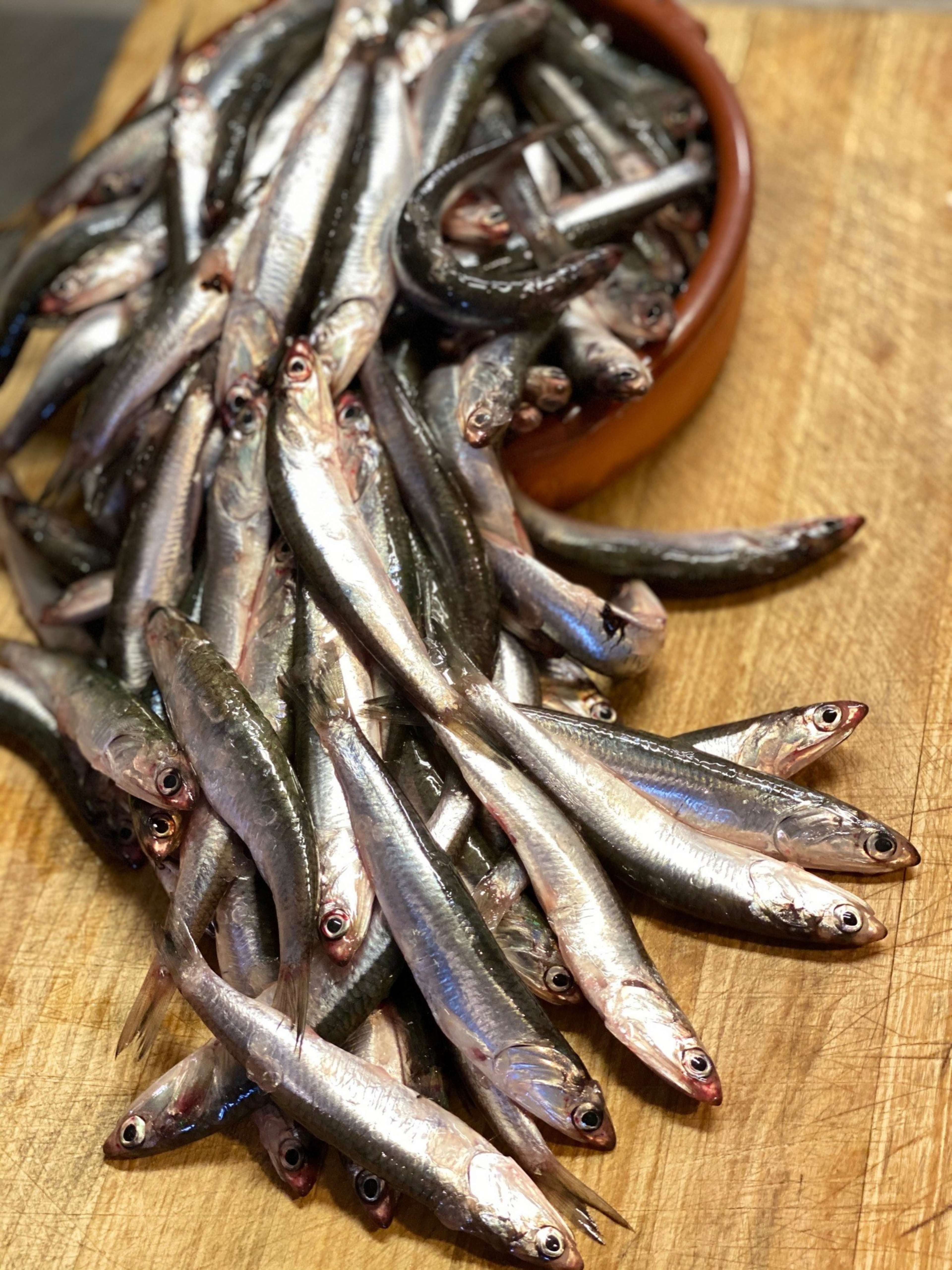 A pile of small, shiny silver fish with open eyes rests on a wooden ...