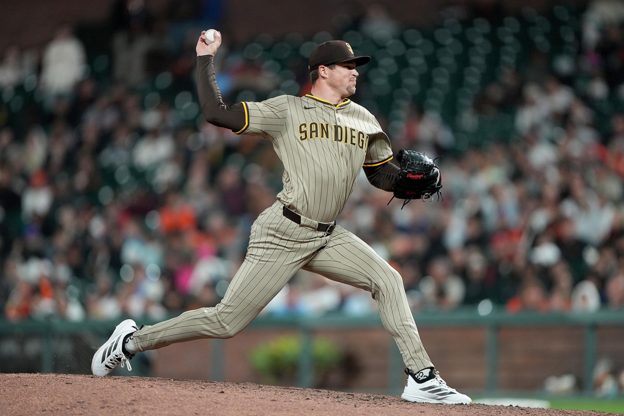 A baseball pitcher in a San Diego uniform is mid-throw on the mound with a blurred crowd in the background.