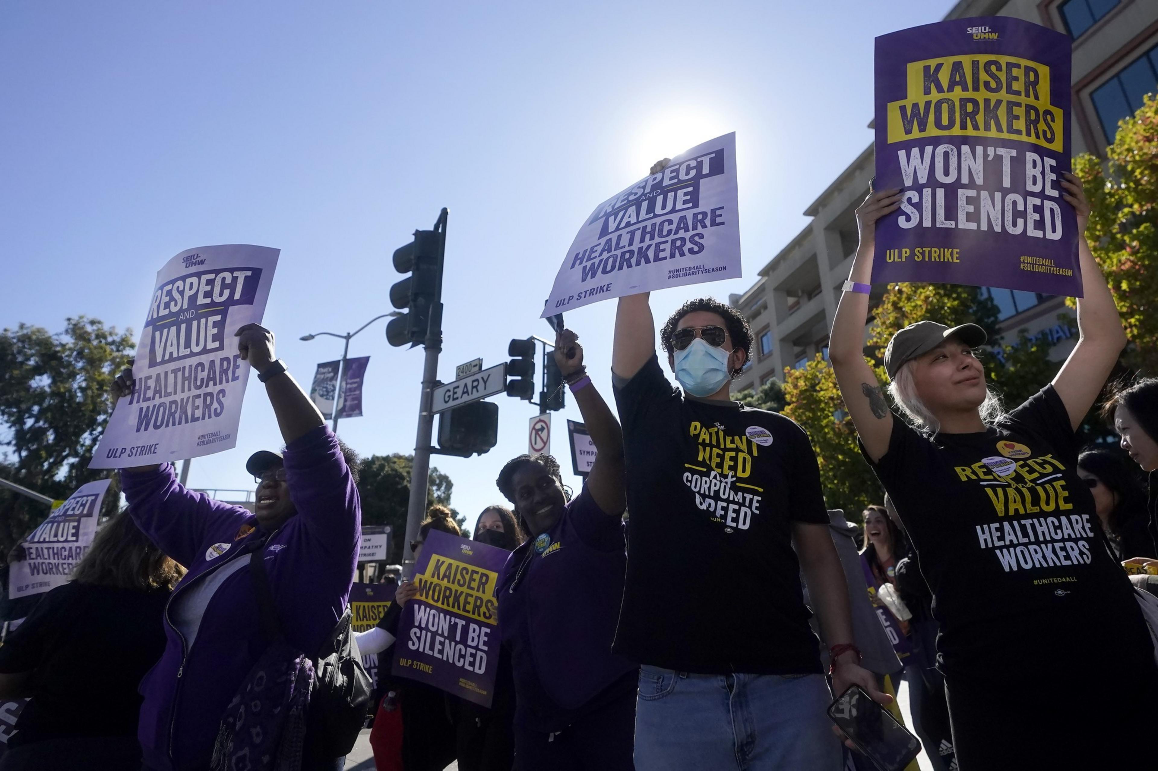 A group of union employees, some wearing masks and sunglasses, hold signs at a public protest.