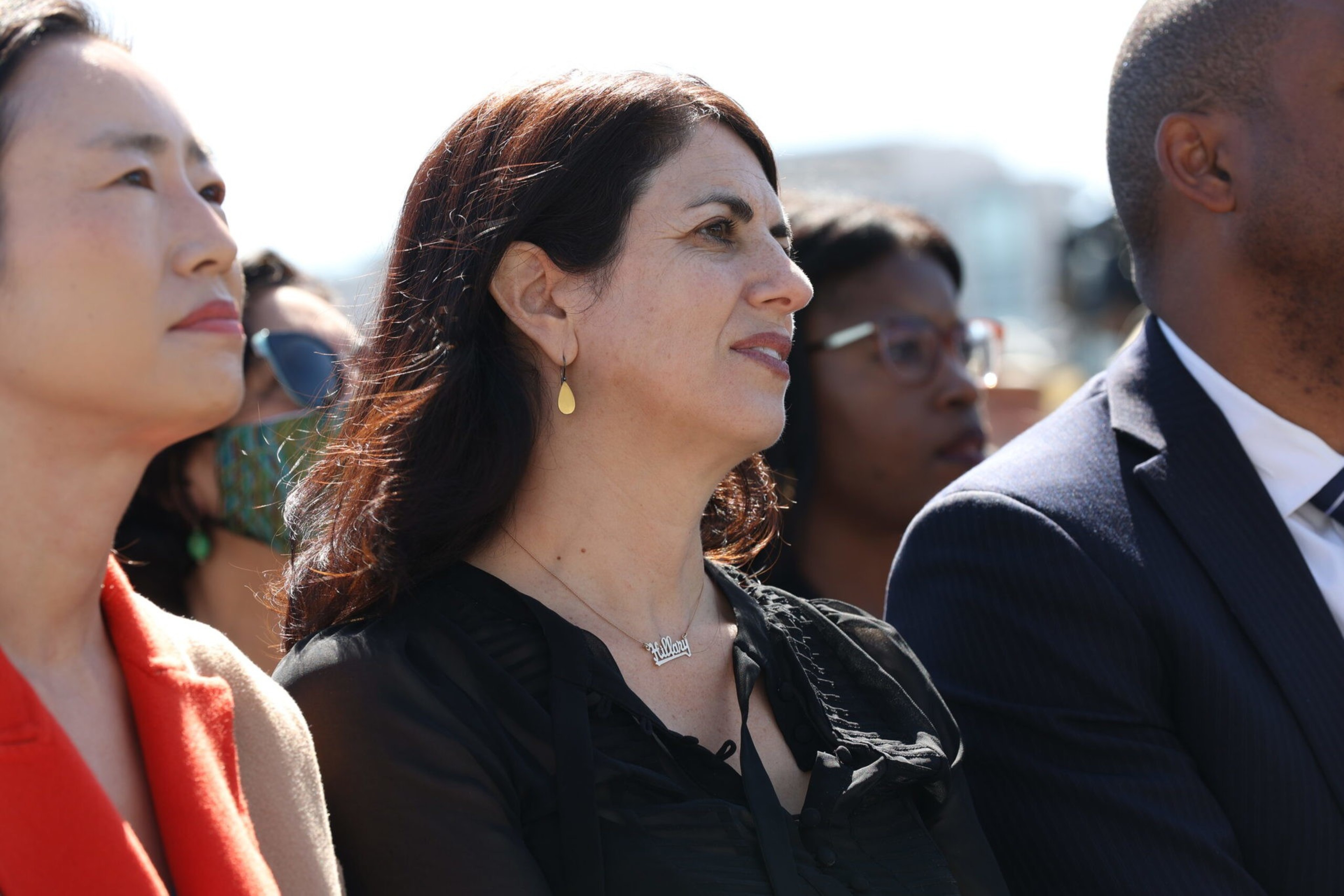 Four people sit side by side outdoors, attentively looking in the same direction, with sunlight illuminating their faces.