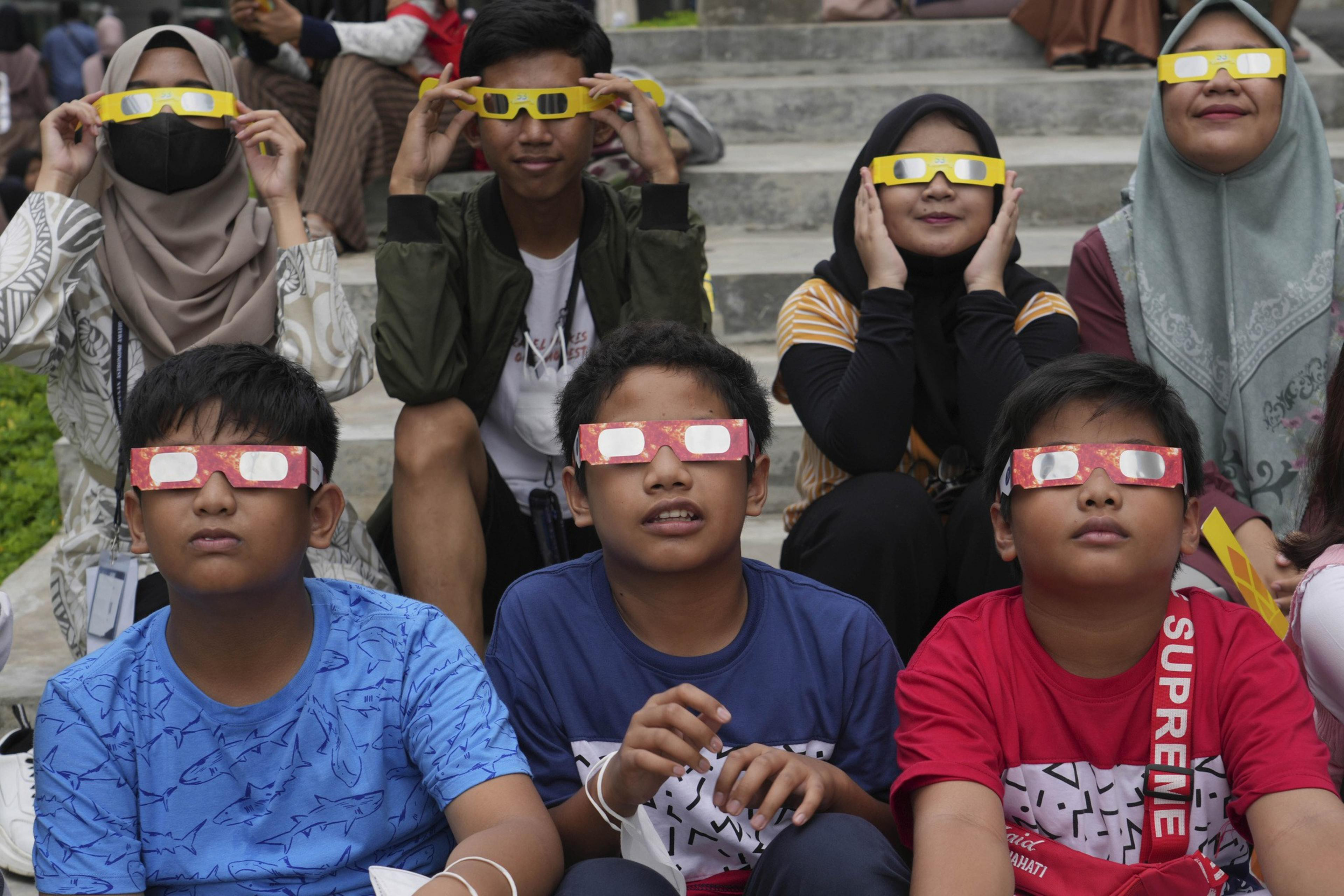 Youths wear protective glasses to watch a hybrid solar eclipse in Jakarta, Indonesia, Thursday, April 20, 2023.