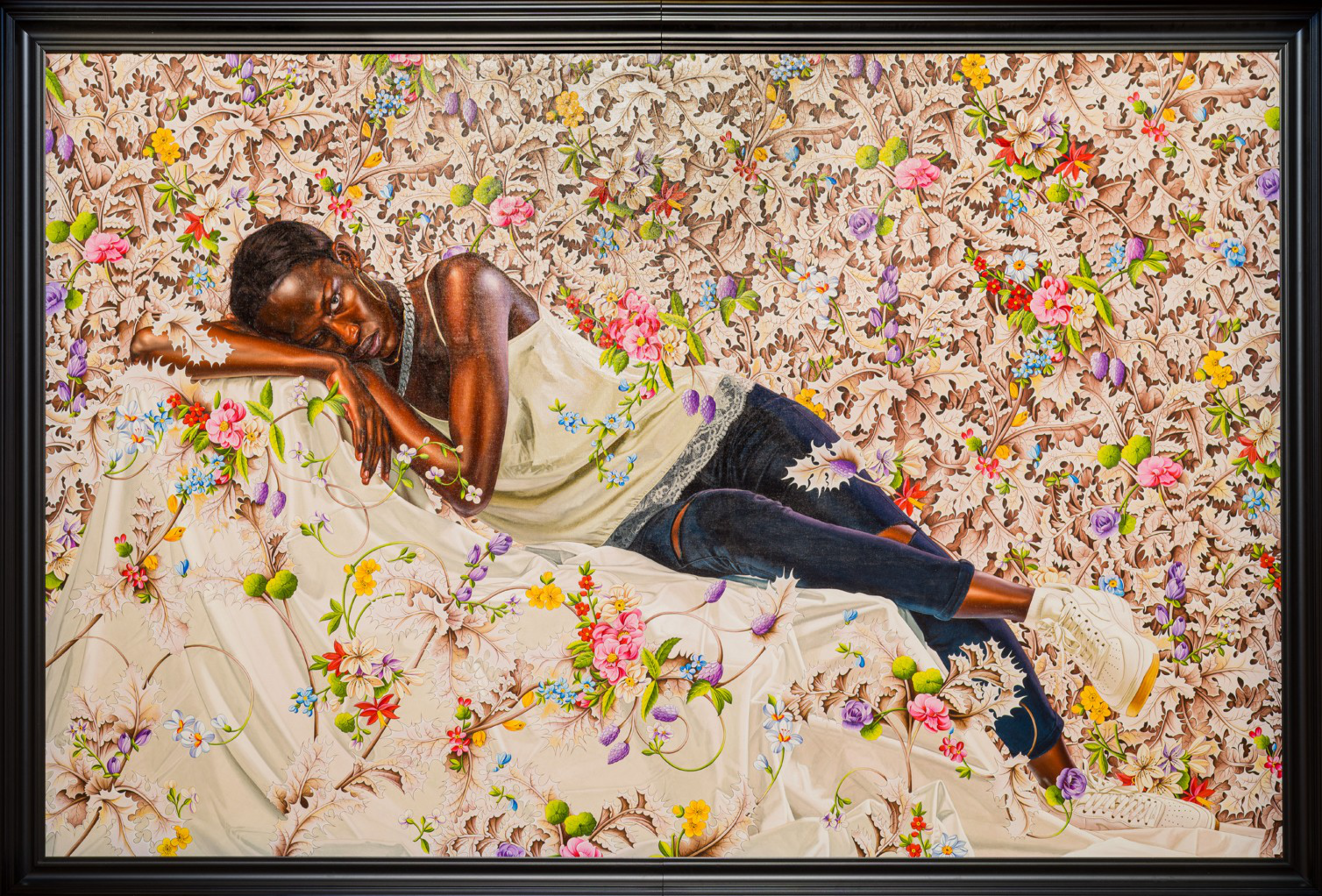 A person wearing a white tank top, dark ripped jeans, and white boots lies sideways with eyes closed on a floral-patterned fabric blending into the background.