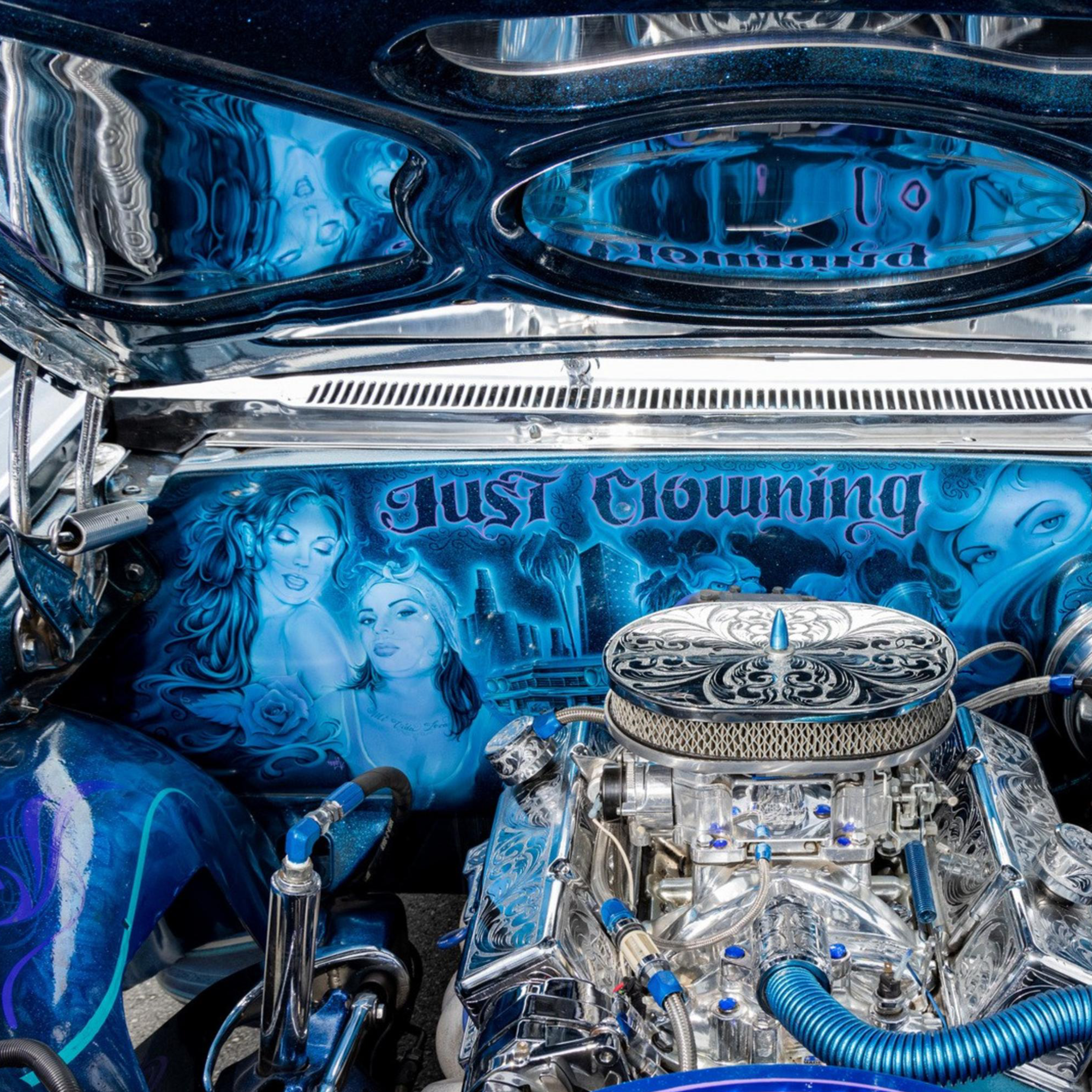 The image shows a customized car engine with detailed silver and blue components, artwork of women, and the phrase &quot;Just Clowning&quot; displayed inside the hood.