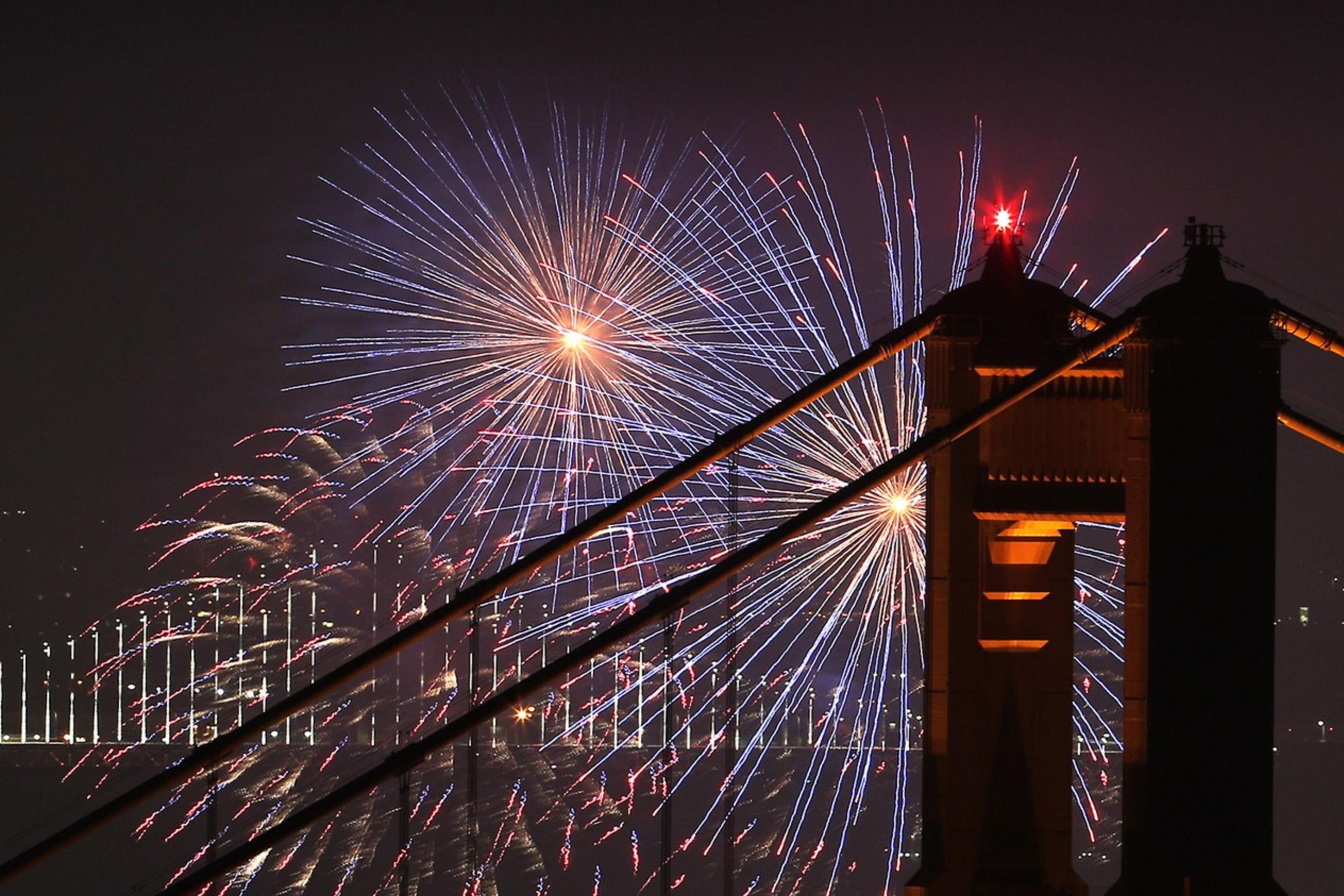 fireworks are shot off in the background of the Golden Gate Bridge.