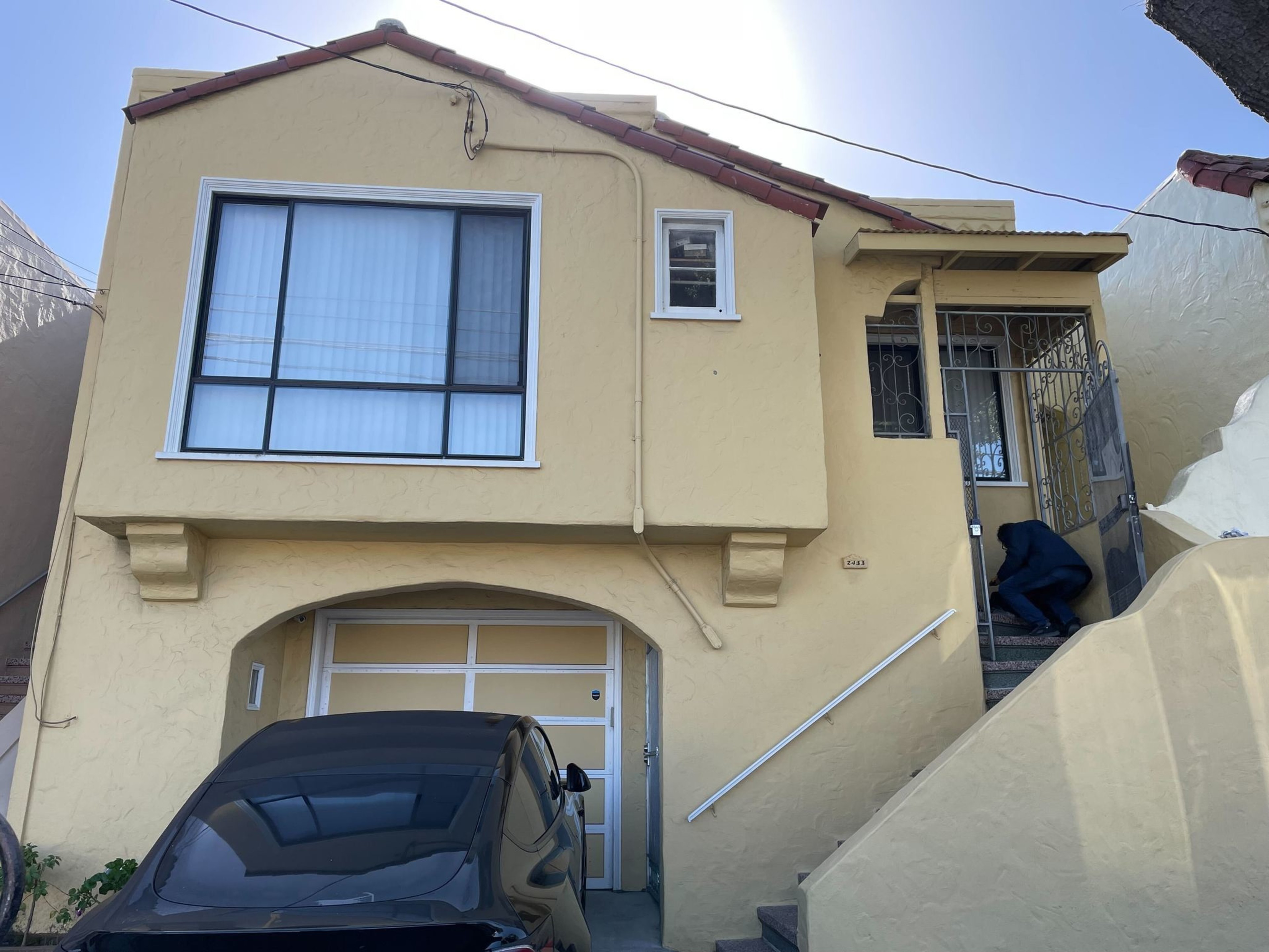 A yellow two-story house with a garage and stairs leading to an entrance, with a car parked in front.