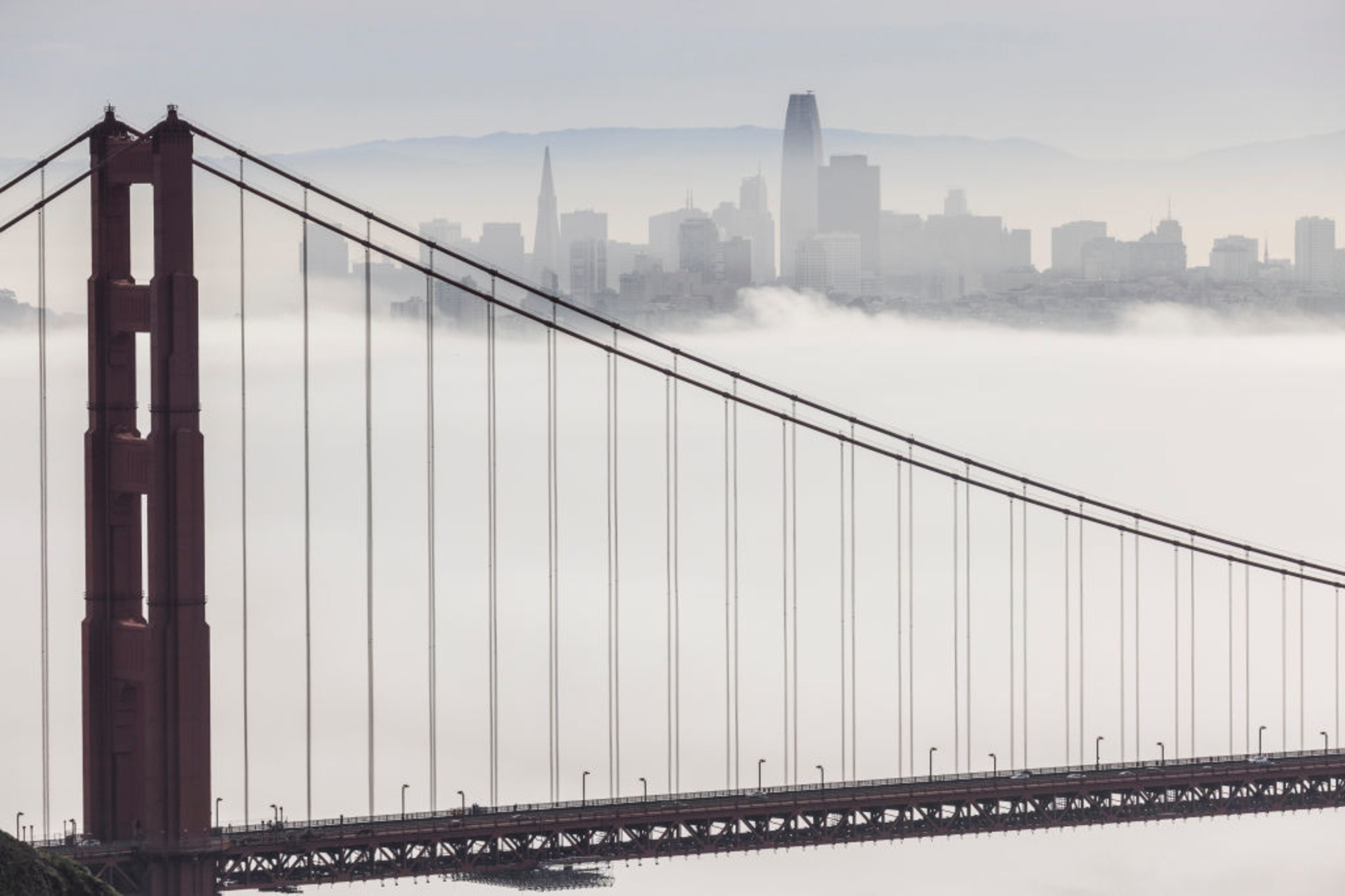 The Golden Gate Bridge stretches across thick fog with San Francisco's skyline faintly visible in the misty background.