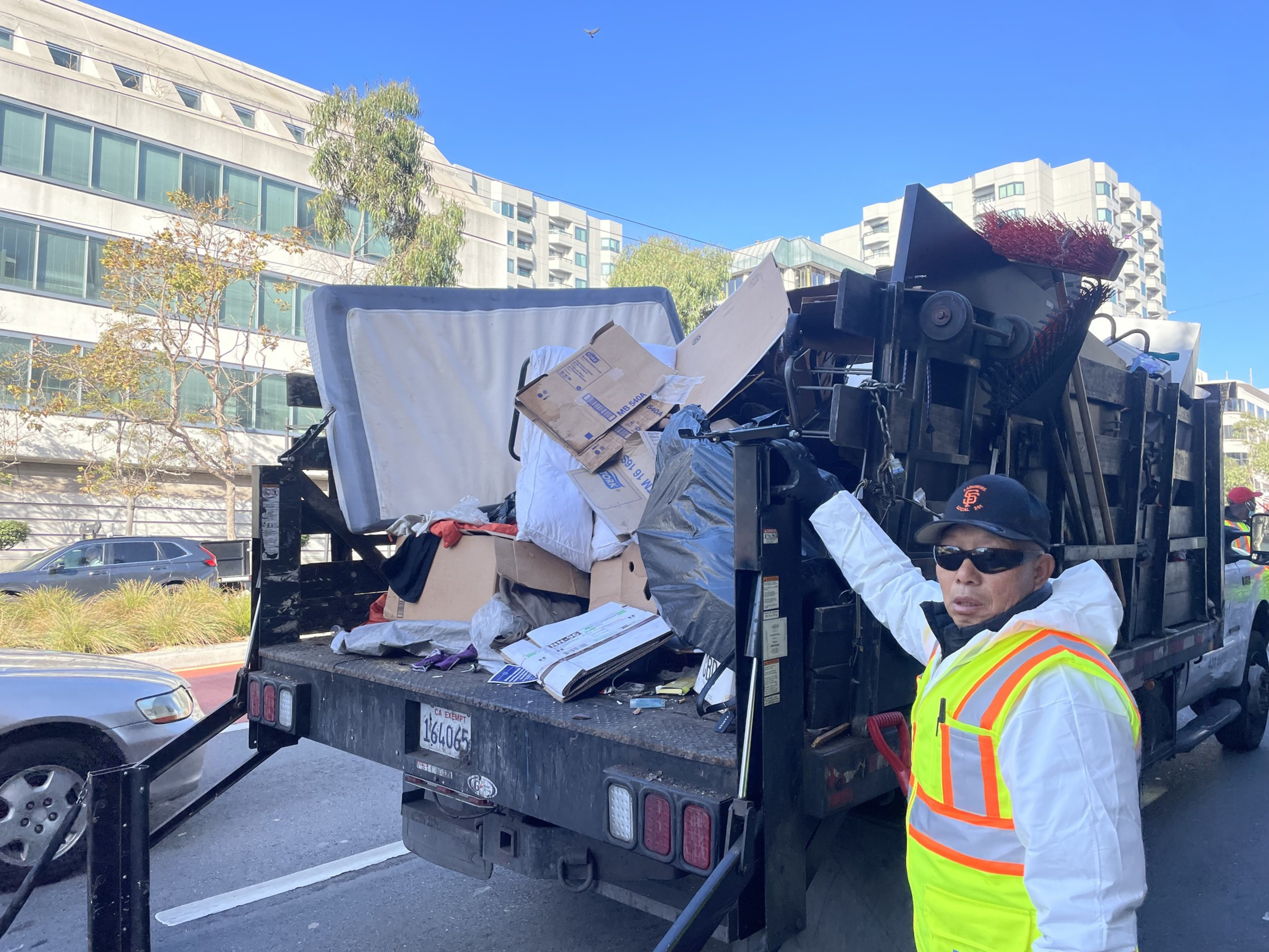 A city employee looks at the camera as he loads unhoused people's items into a truck.