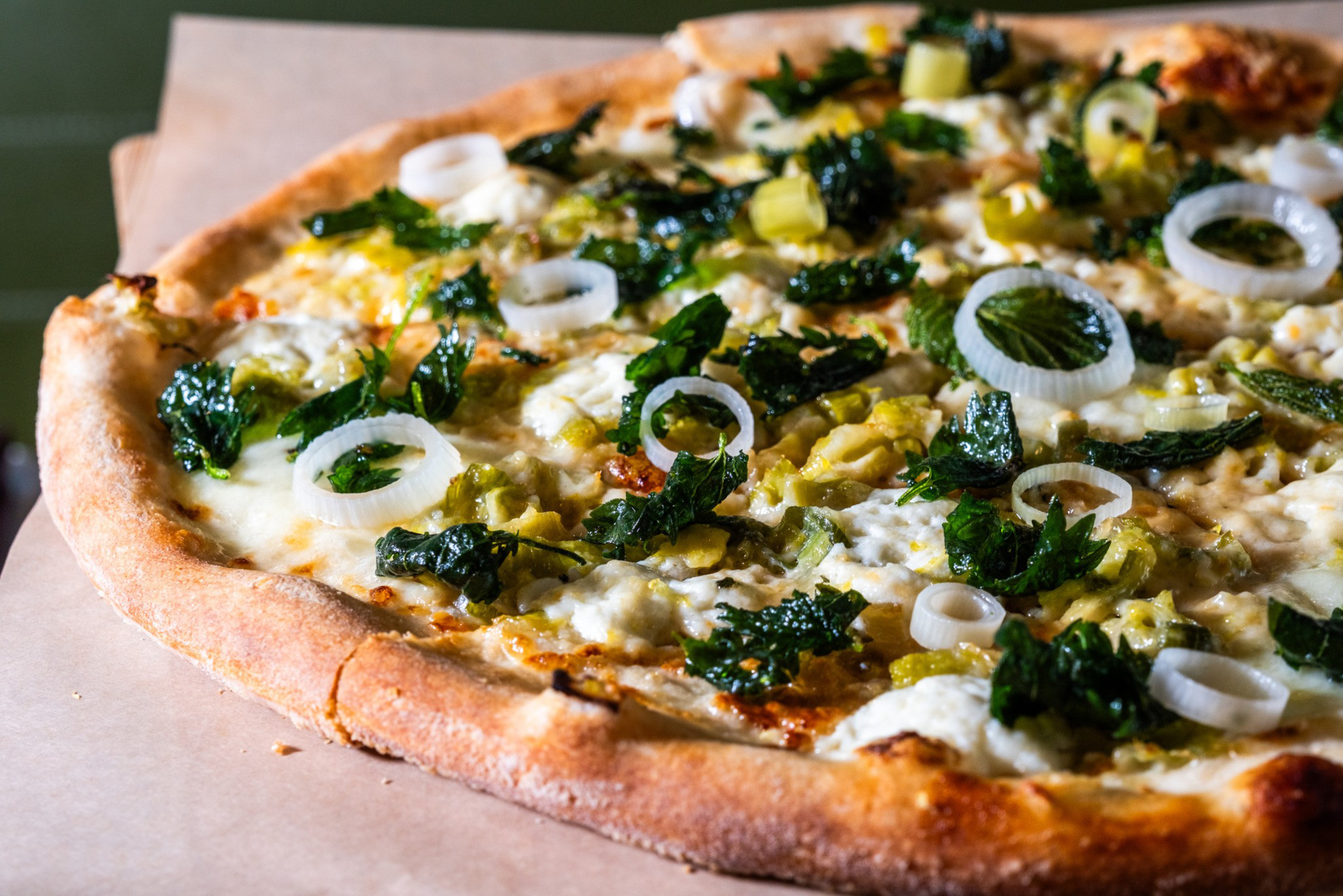 A pizza topped with melted cheese, vibrant green leaves, sliced onions, and bits of yellow-green vegetables on a golden-brown, crispy crust.