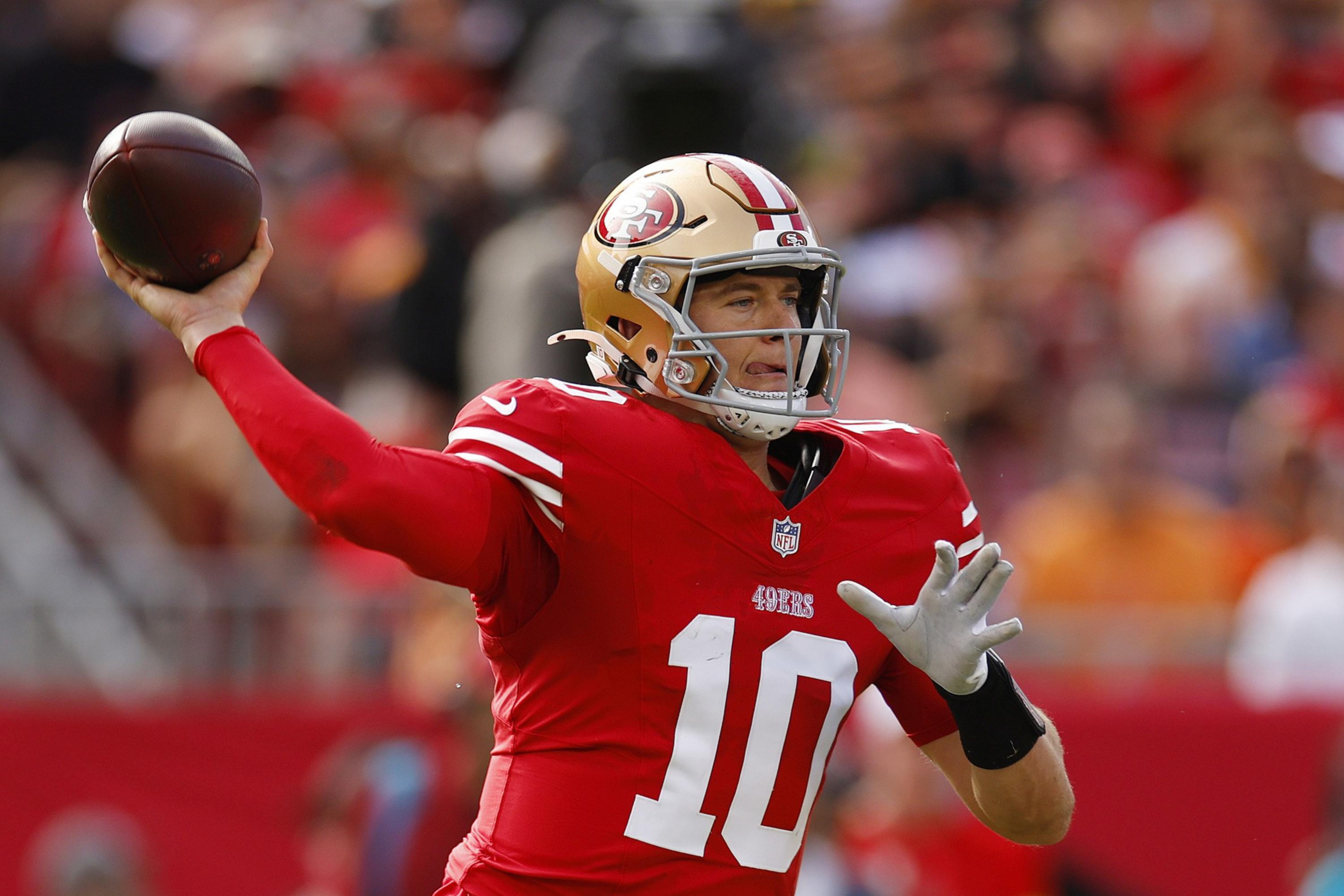 A football player in a red San Francisco 49ers jersey, number 10, is throwing a football during a game.