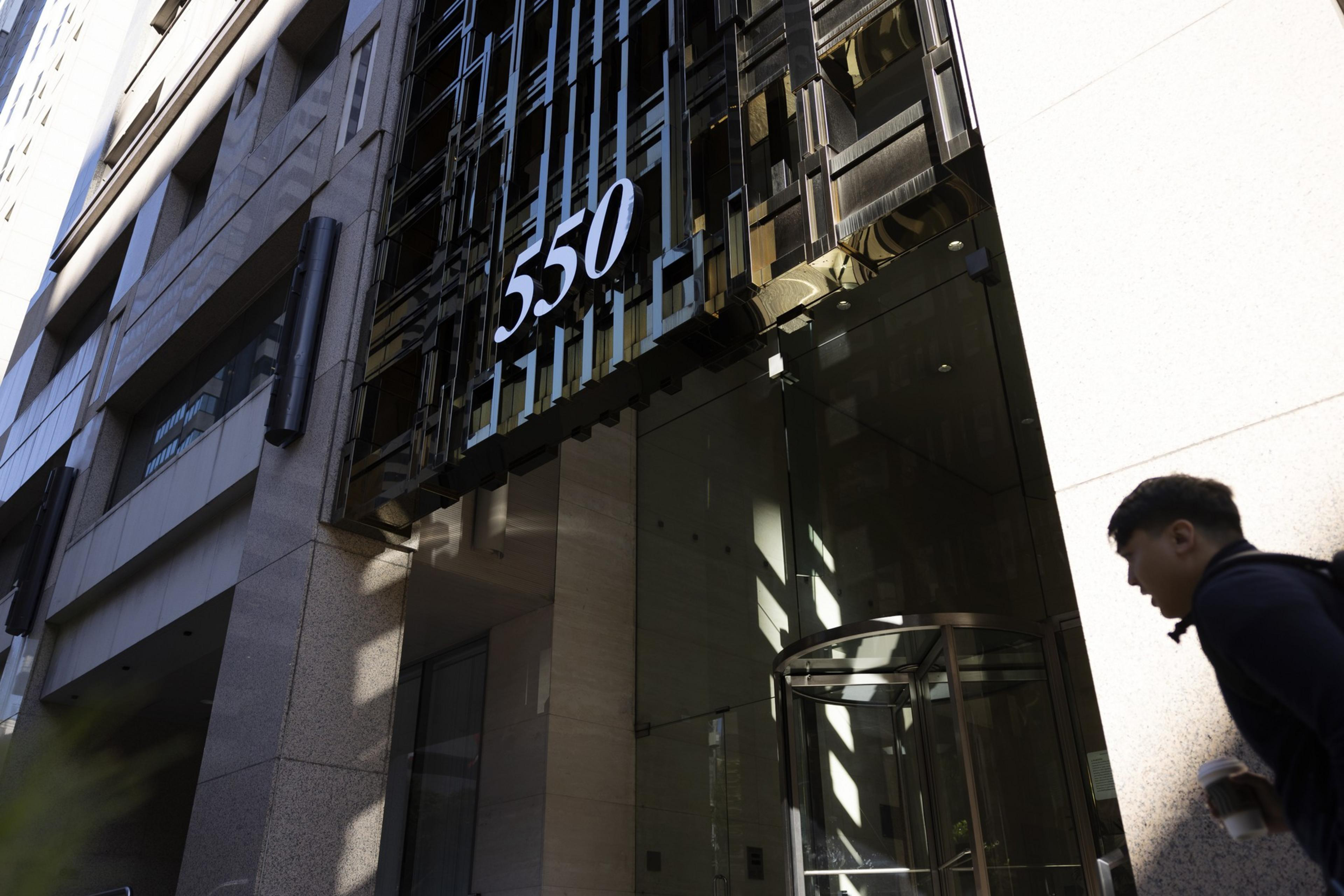A modern building entrance features a revolving door beneath the large number "550," with a person walking by holding a drink.