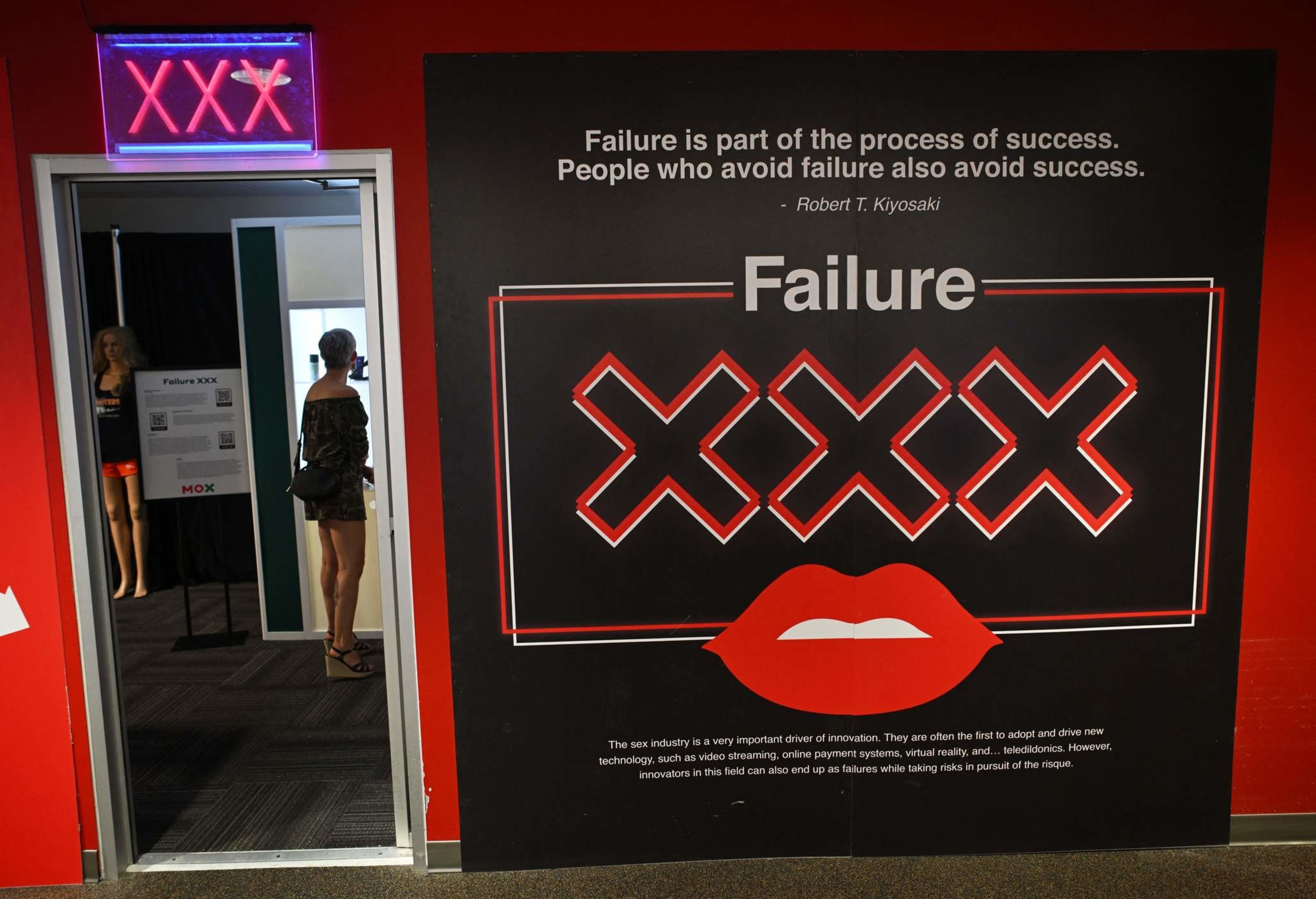 A doorway labeled with a neon &quot;XXX&quot; sign opens to a room with a mannequin and a person. A wall displays &quot;Failure&quot; and a quote about success and failure.