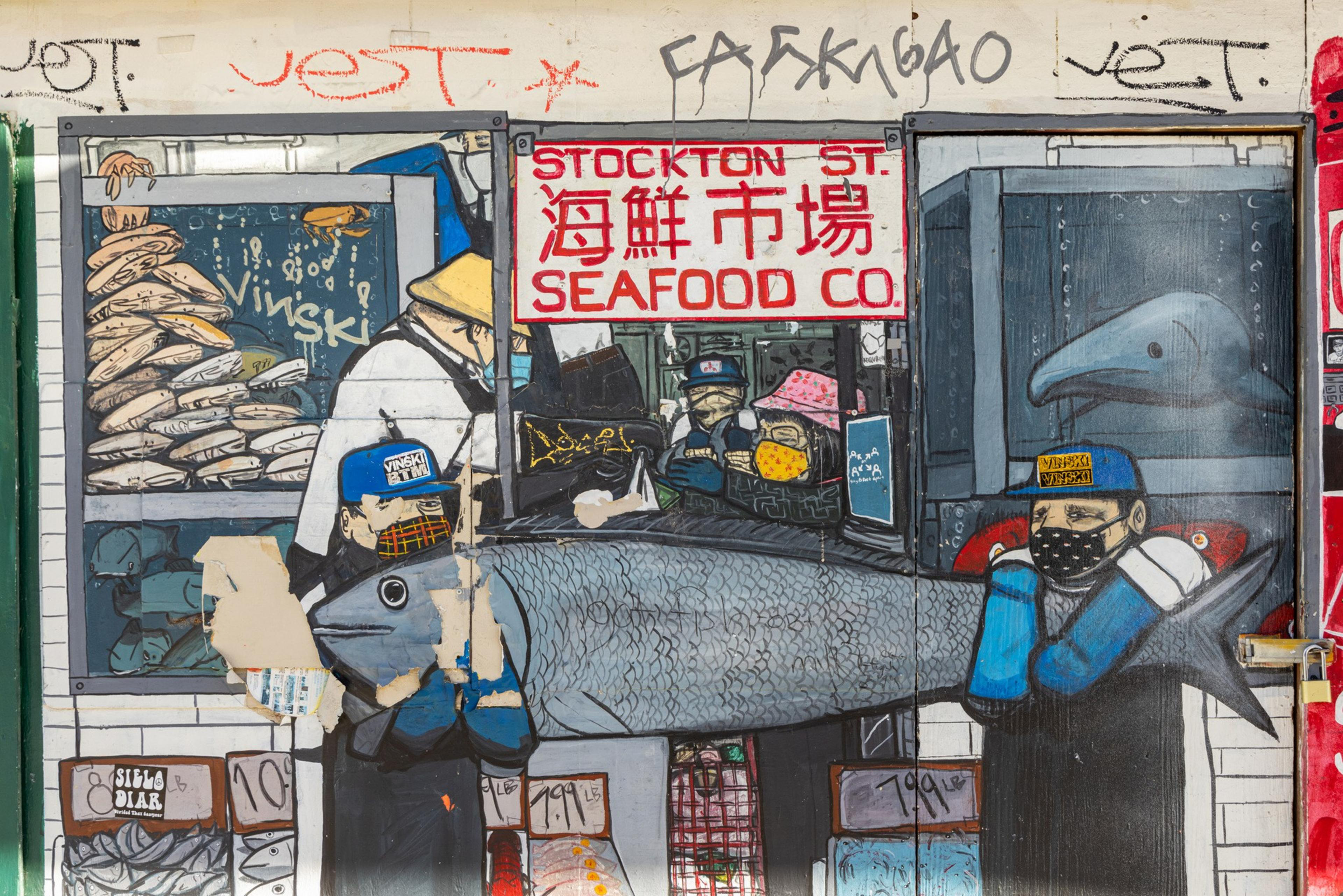 The image shows a colorful mural depicting a seafood market scene, with workers handling a large fish. The setting includes store signs and various seafood items.