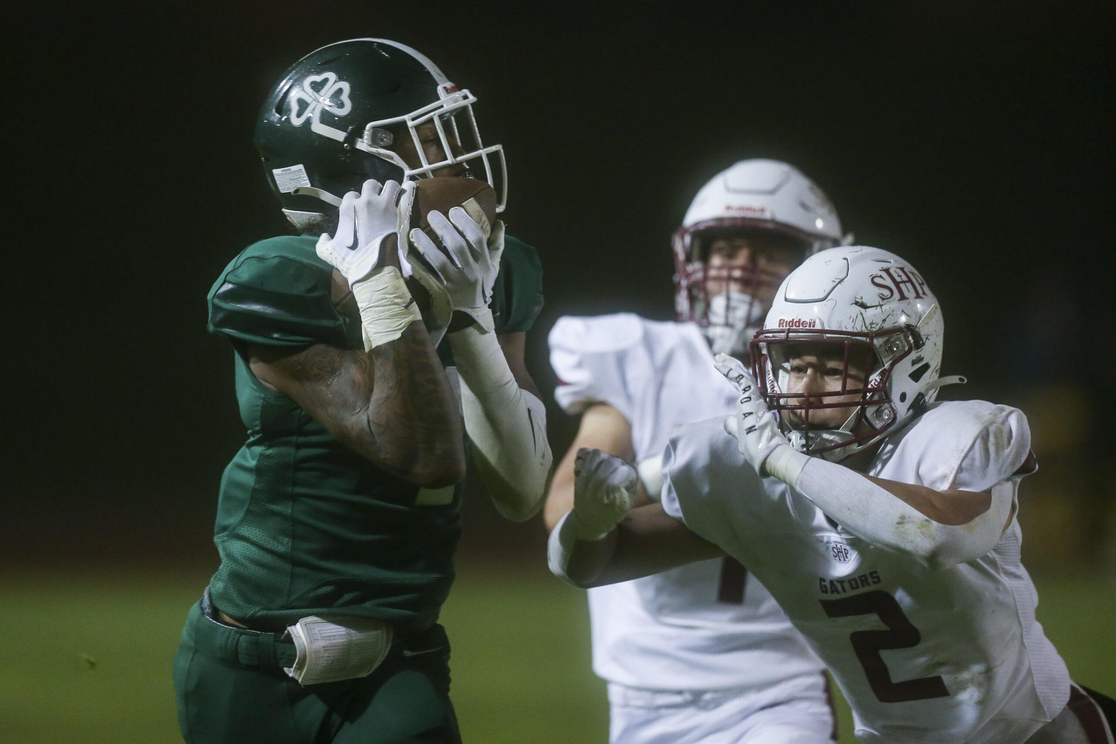 A football player in a green uniform catches the ball while two players in white uniforms close in to defend.