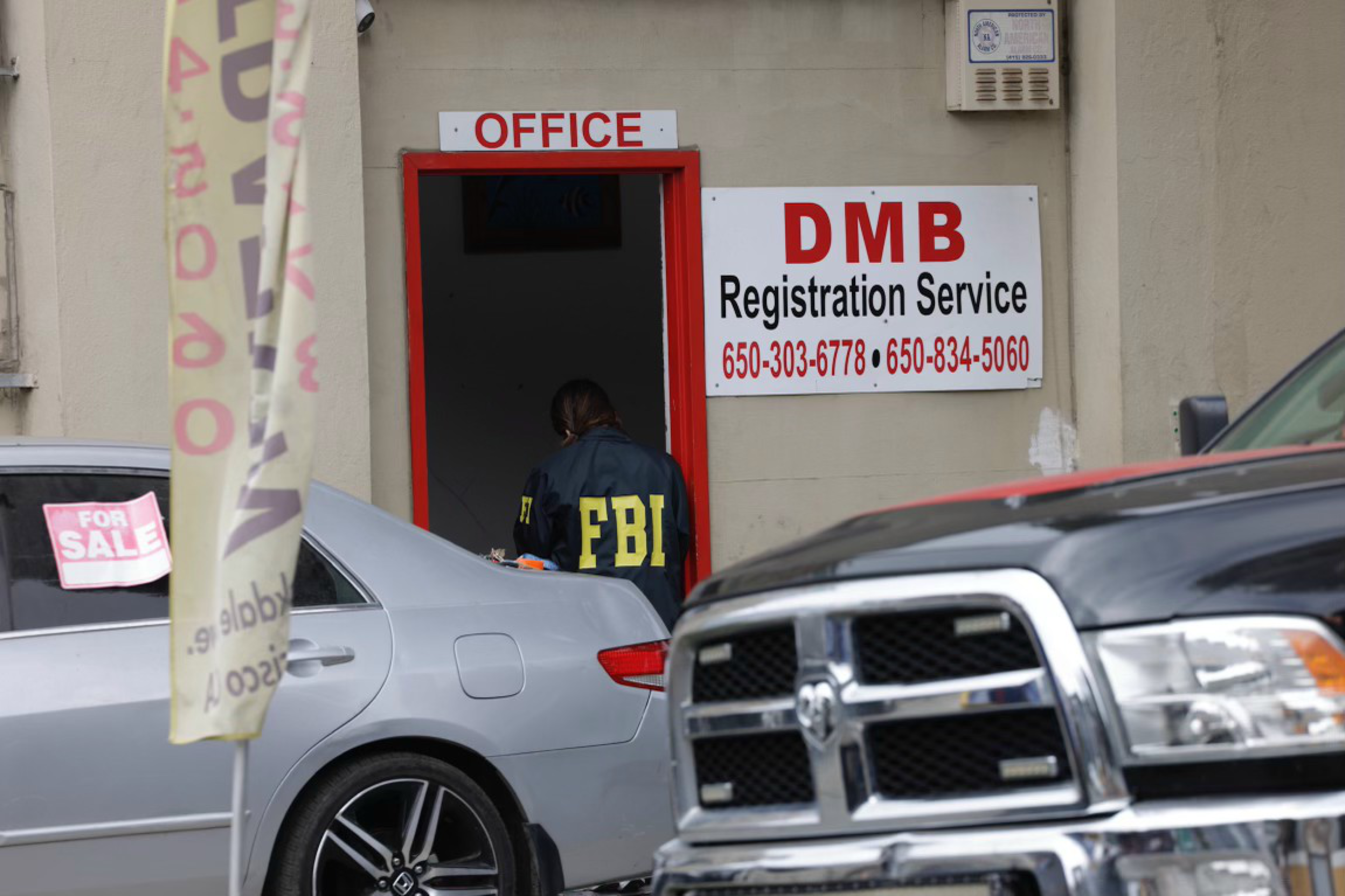 A man in a jacket that says FBI on the back is seen standing in the doorway of a small business.