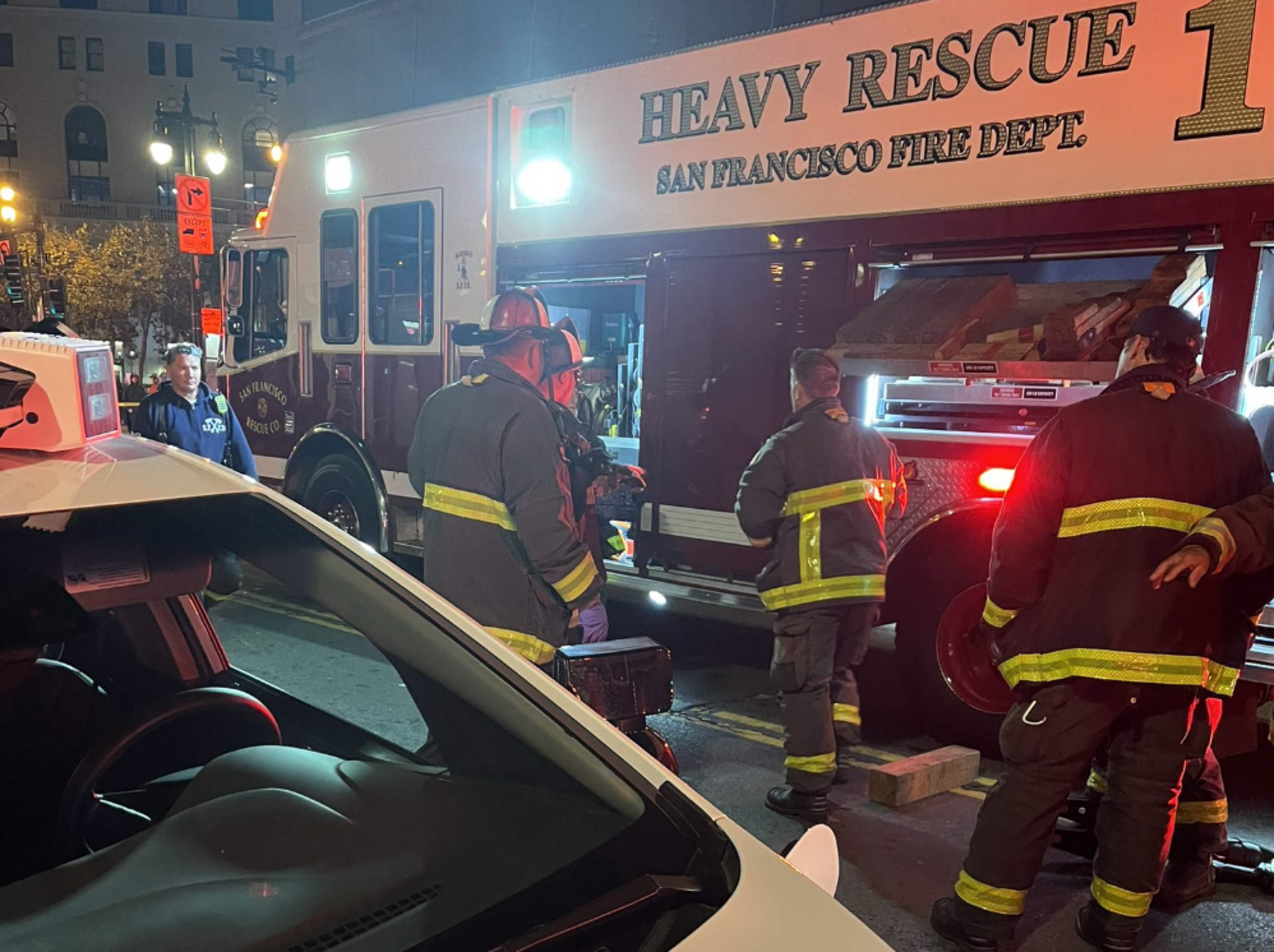 Firefighters in dark-colored gear with fluorescent stripes stand near a department heavy rescue vehicle.