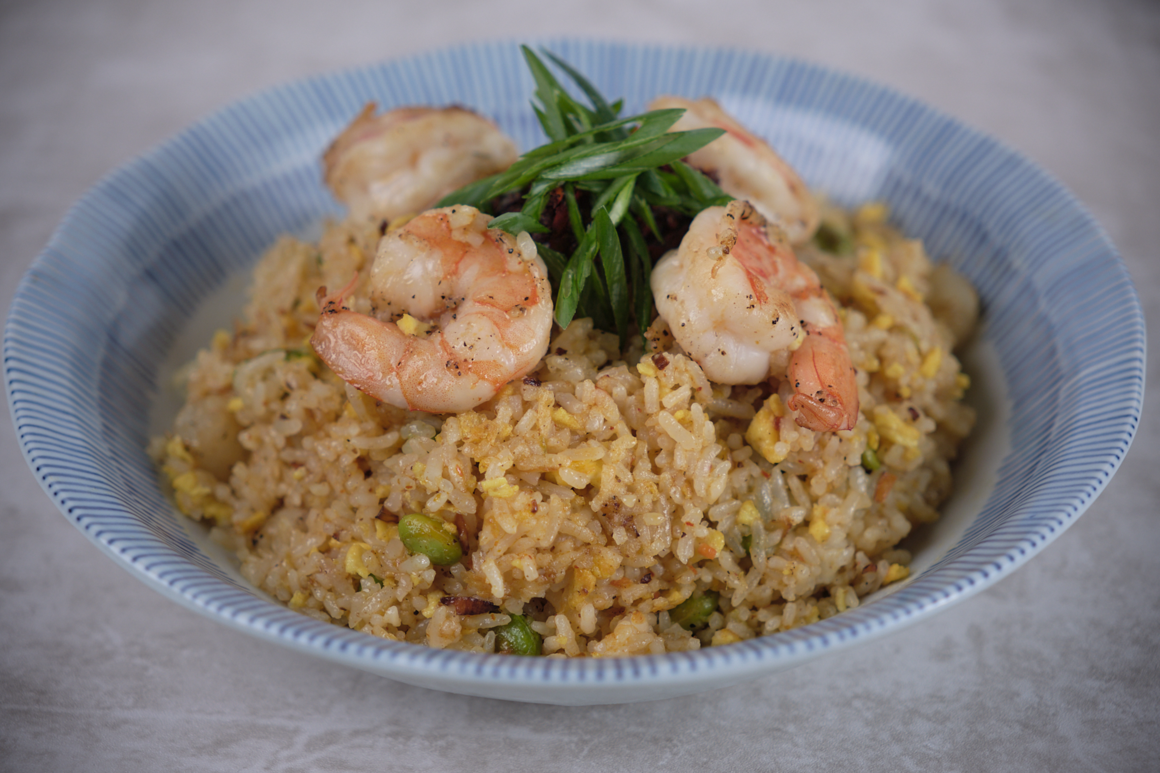 Fried rice with peas, scrambled egg, and grilled shrimp, garnished with sliced green onions, served in a blue and white bowl.