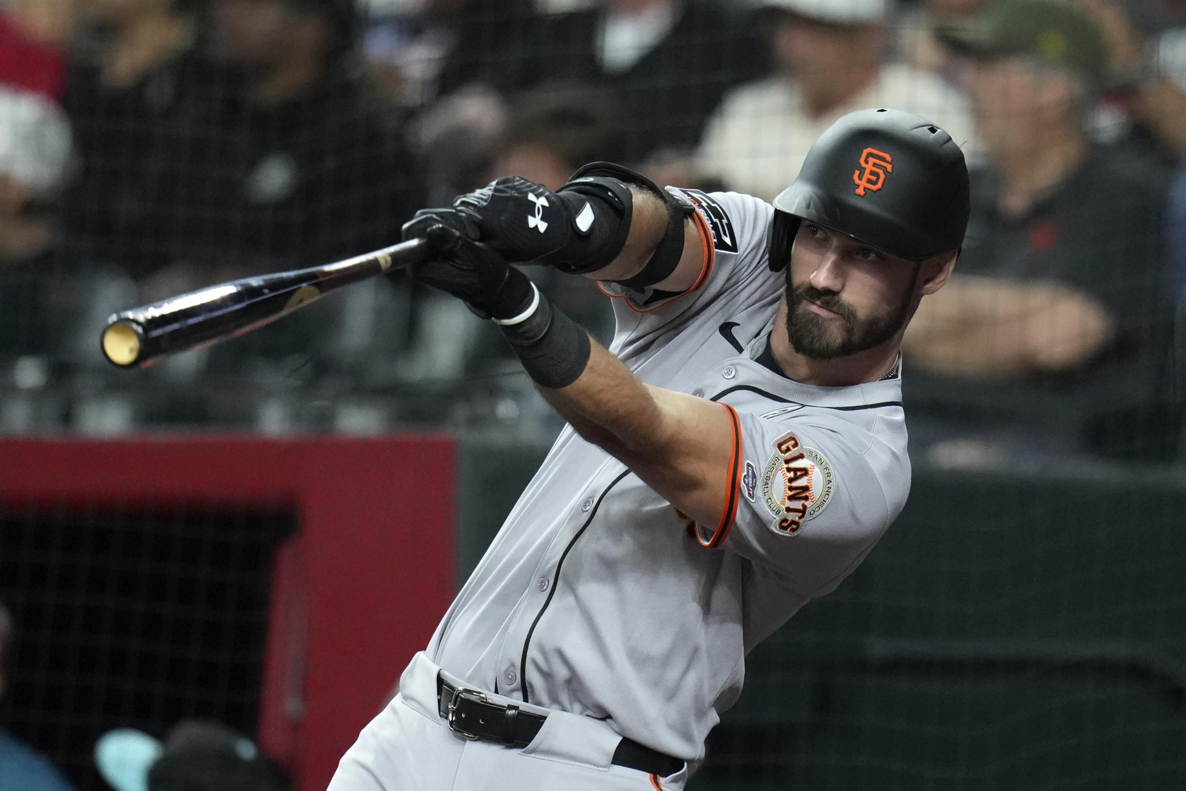 A baseball player wearing a San Francisco Giants uniform swings a bat during a game, focusing intently on the ball.