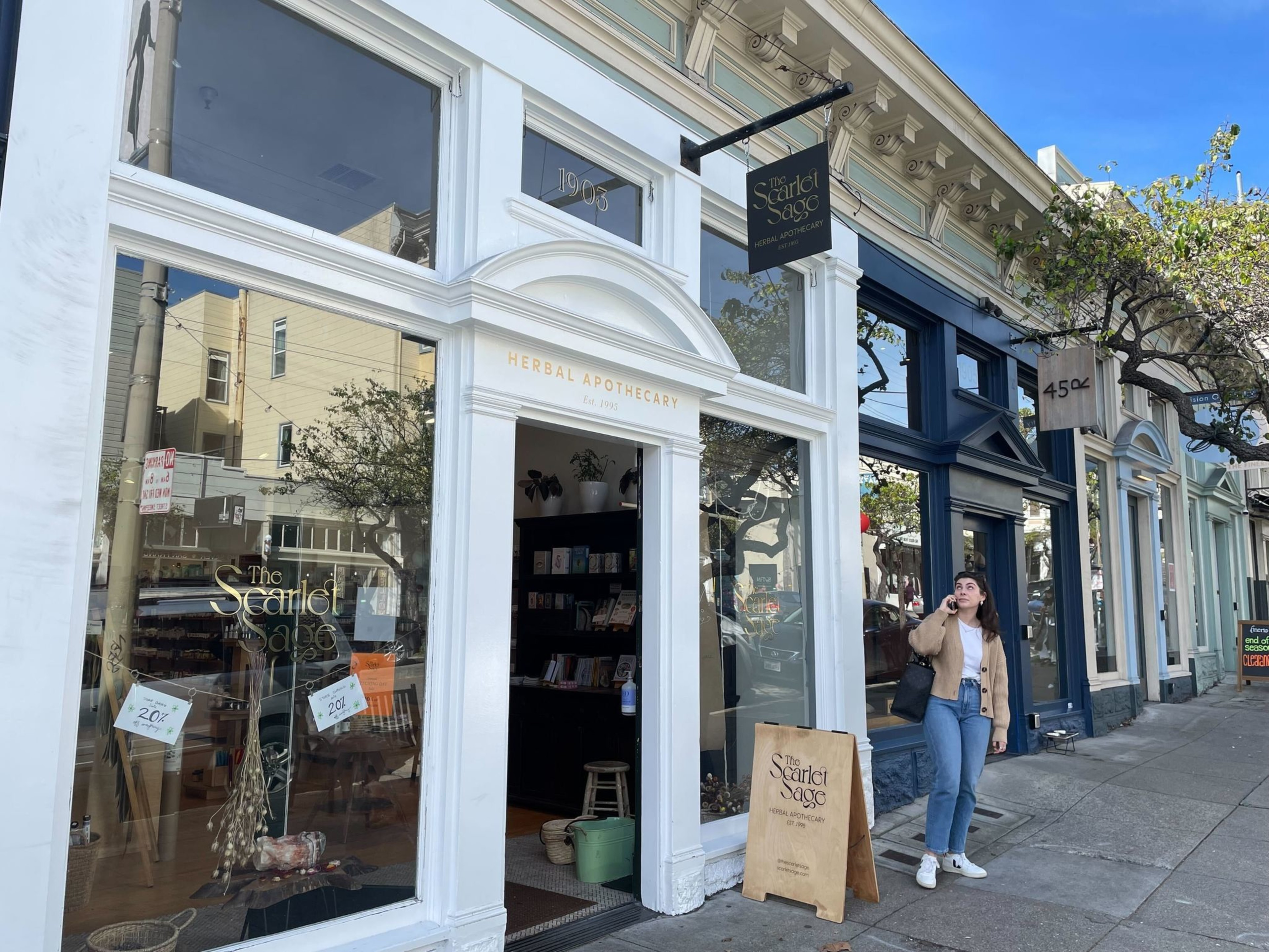 A storefront is seen along a sidewalk, with a person looking at a sign hanging above.