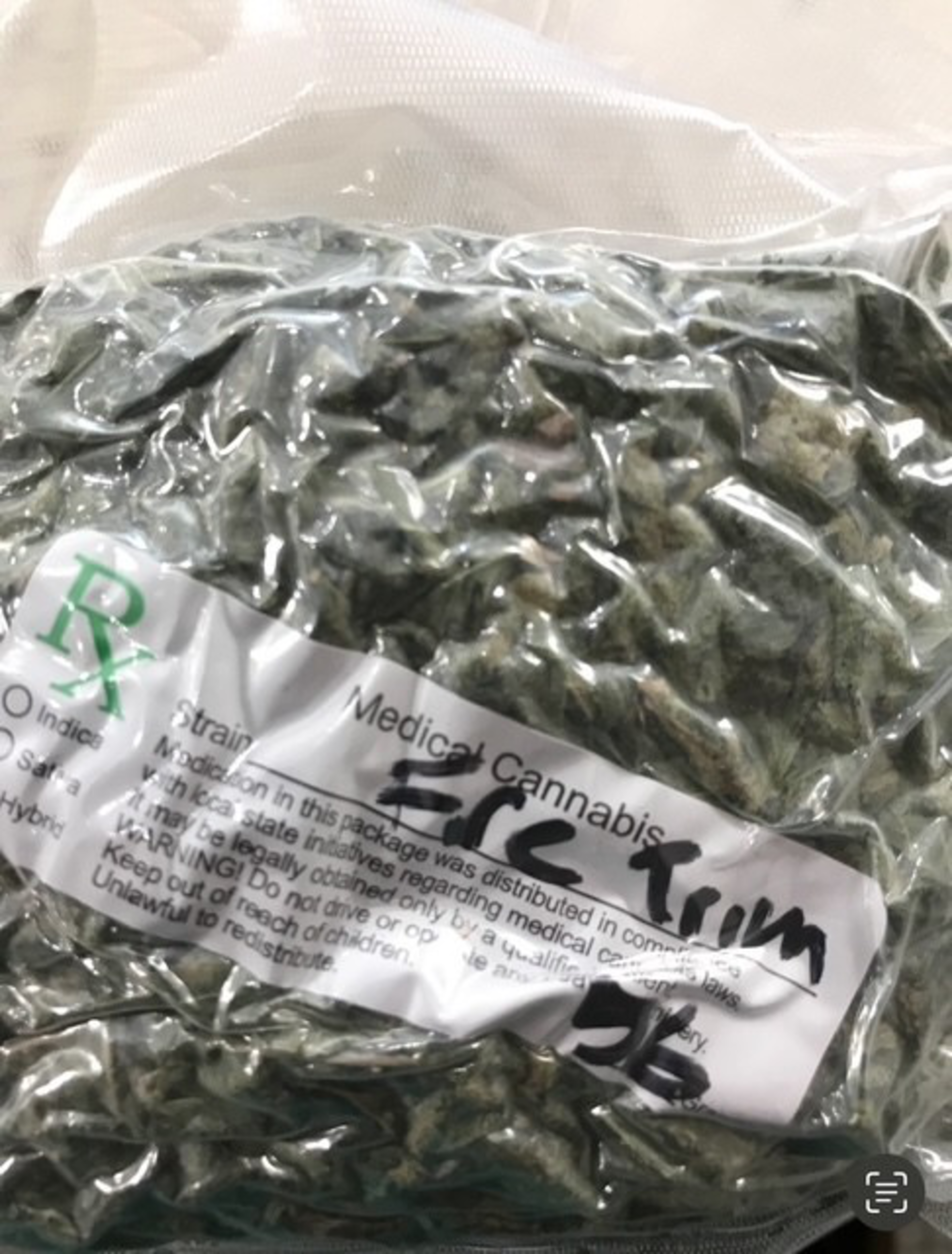 The image shows a clear bag filled with green plant material labeled &quot;Medical Cannabis.&quot; The label includes strain information and usage warnings.