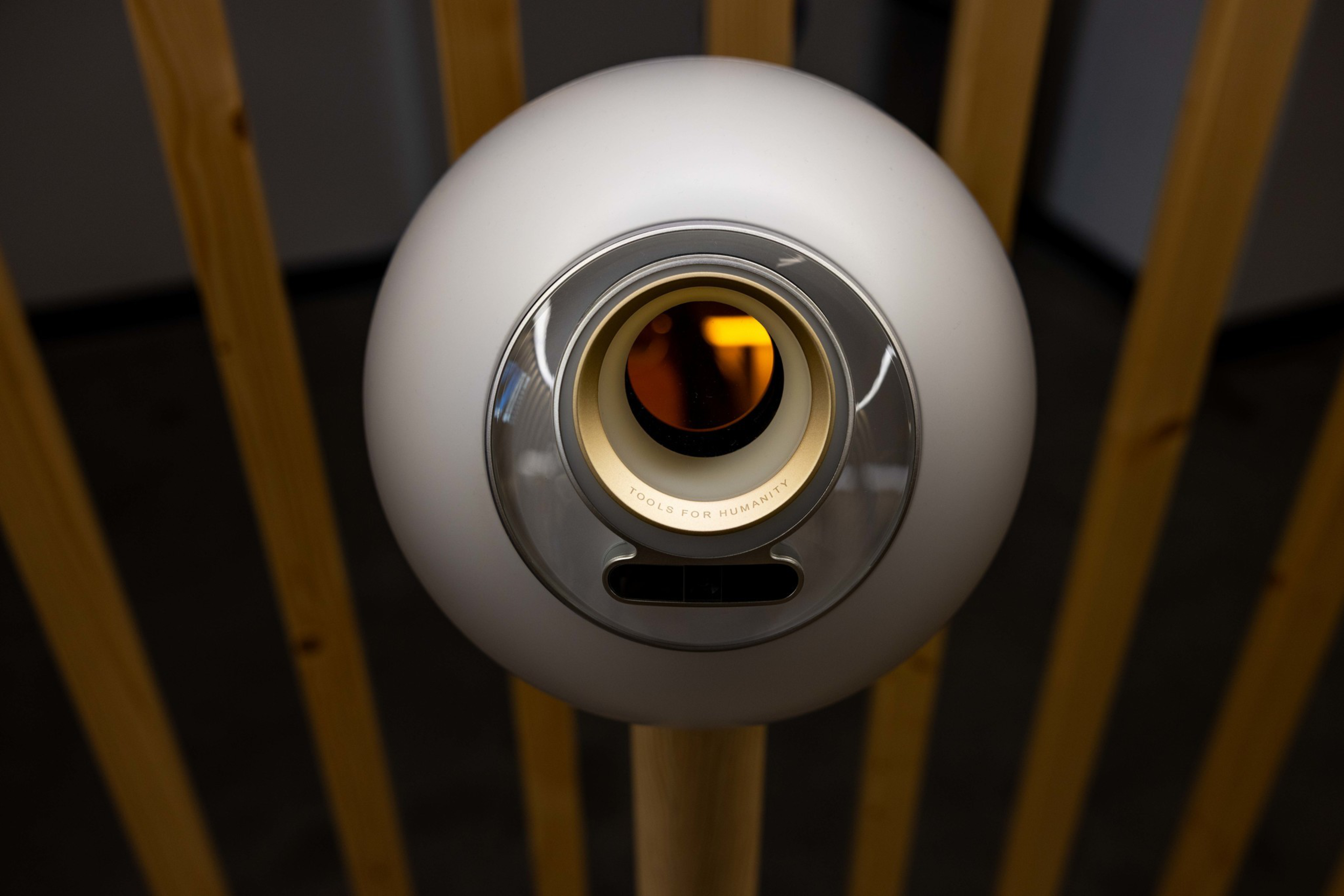 A spherical, white device with a circular opening labeled &acirc;TOOLS FOR HUMANITY&acirc; is mounted on a wooden stand against a background of vertical wooden slats.