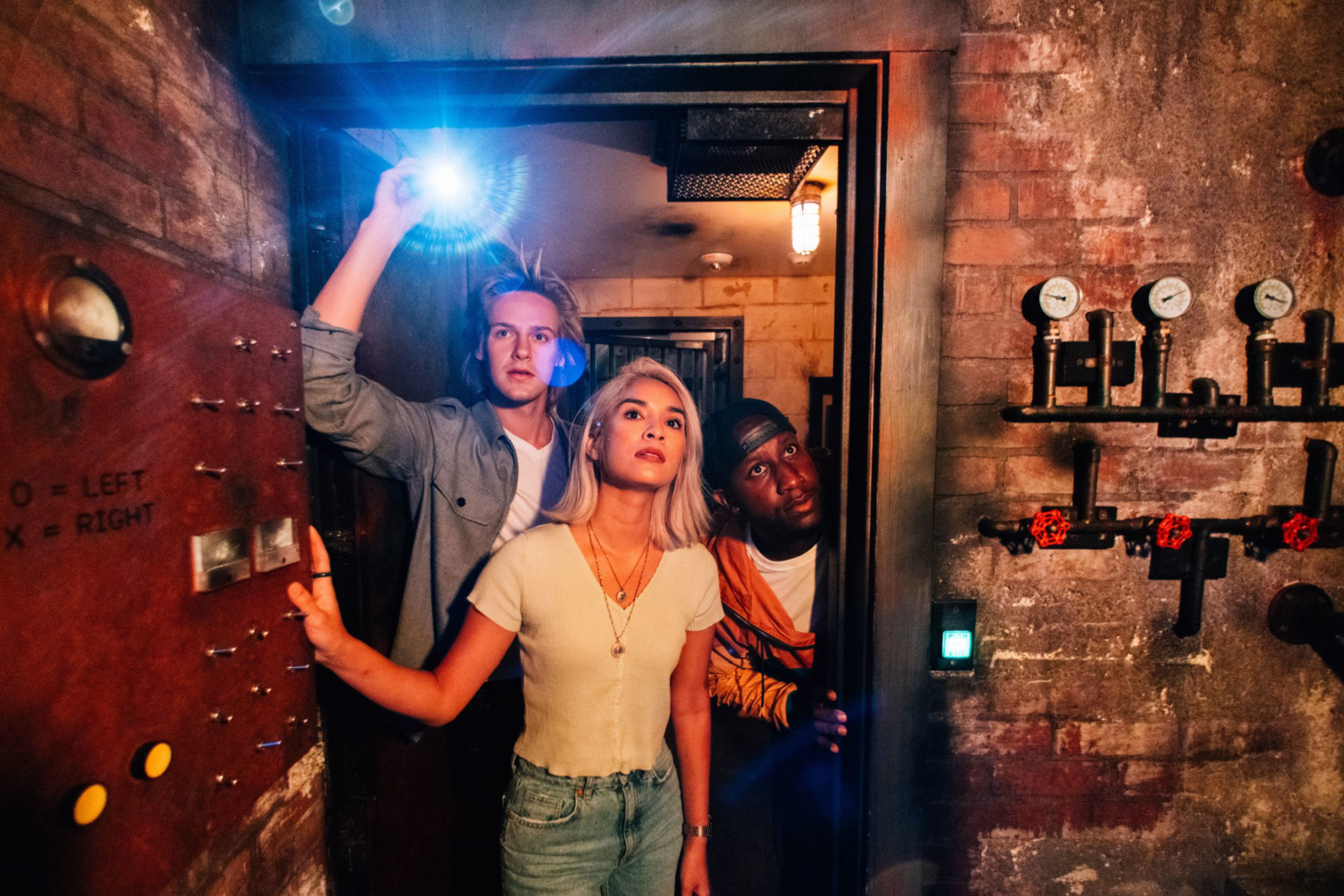 Three young people peer through a doorway in an underground basement space.