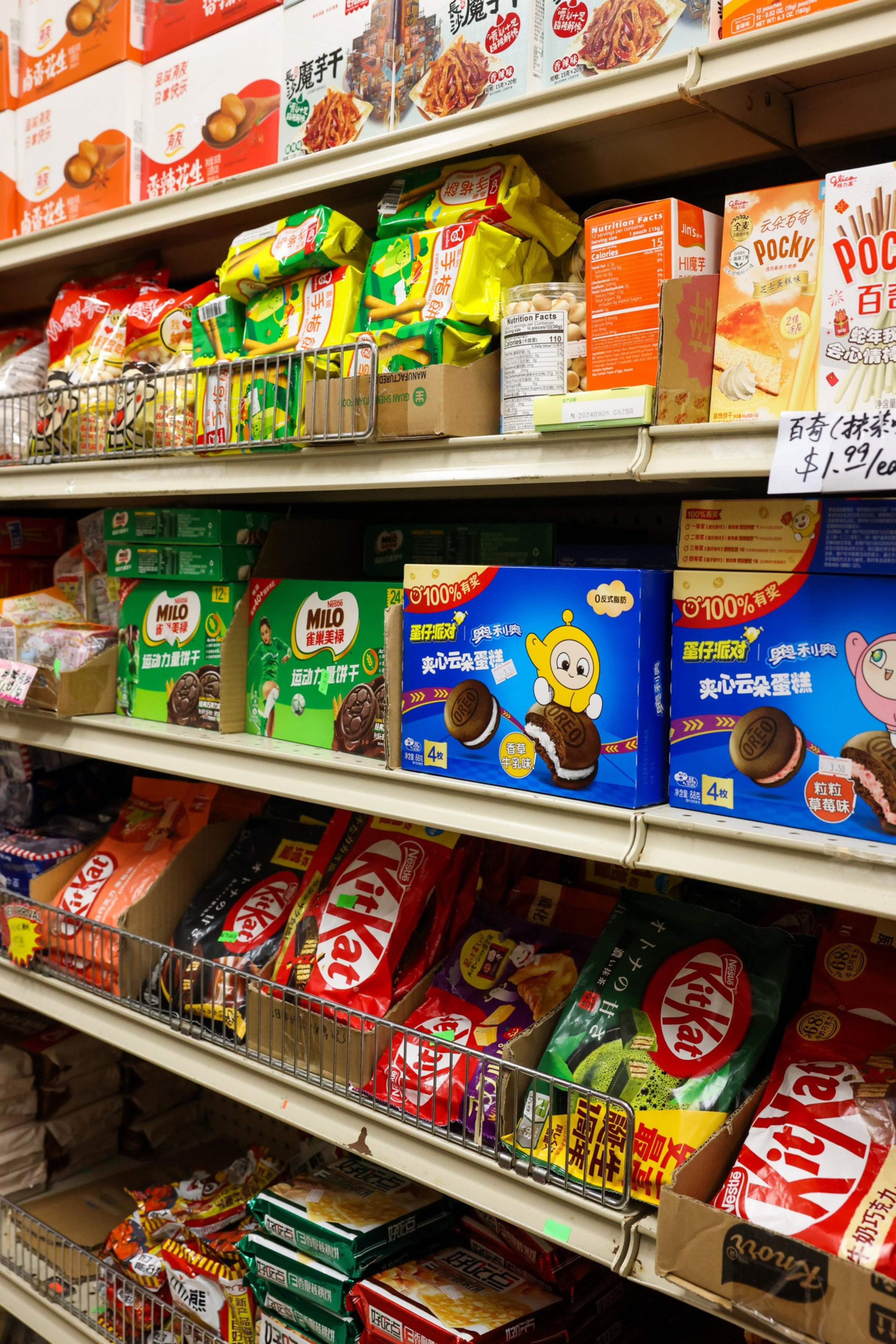 The image shows supermarket shelves stocked with various snacks, including KitKats, Pocky, and other branded goods in colorful packaging.