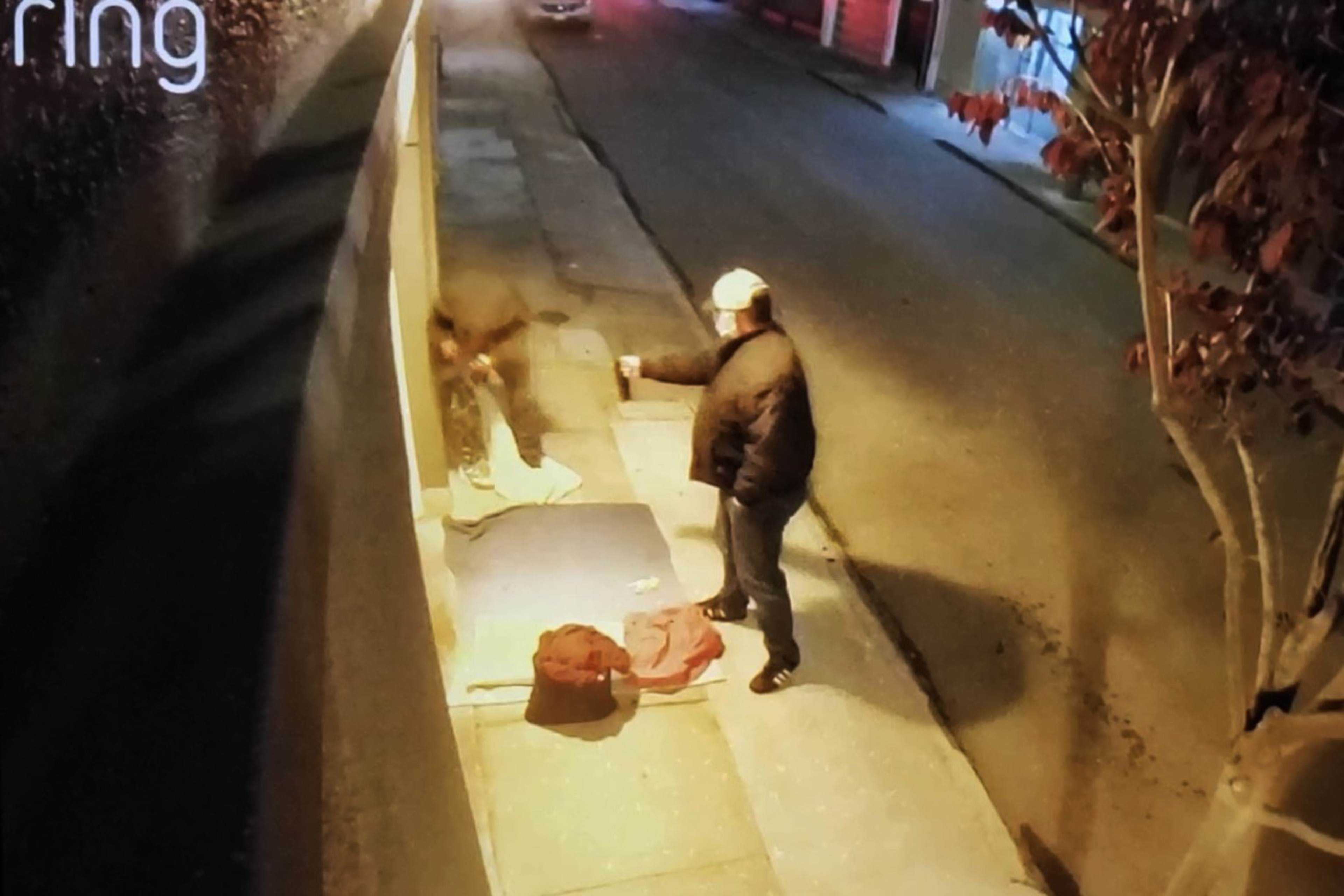 A video surveillance camera captures a man in black coat aiming a spray can at another man on a city street. 