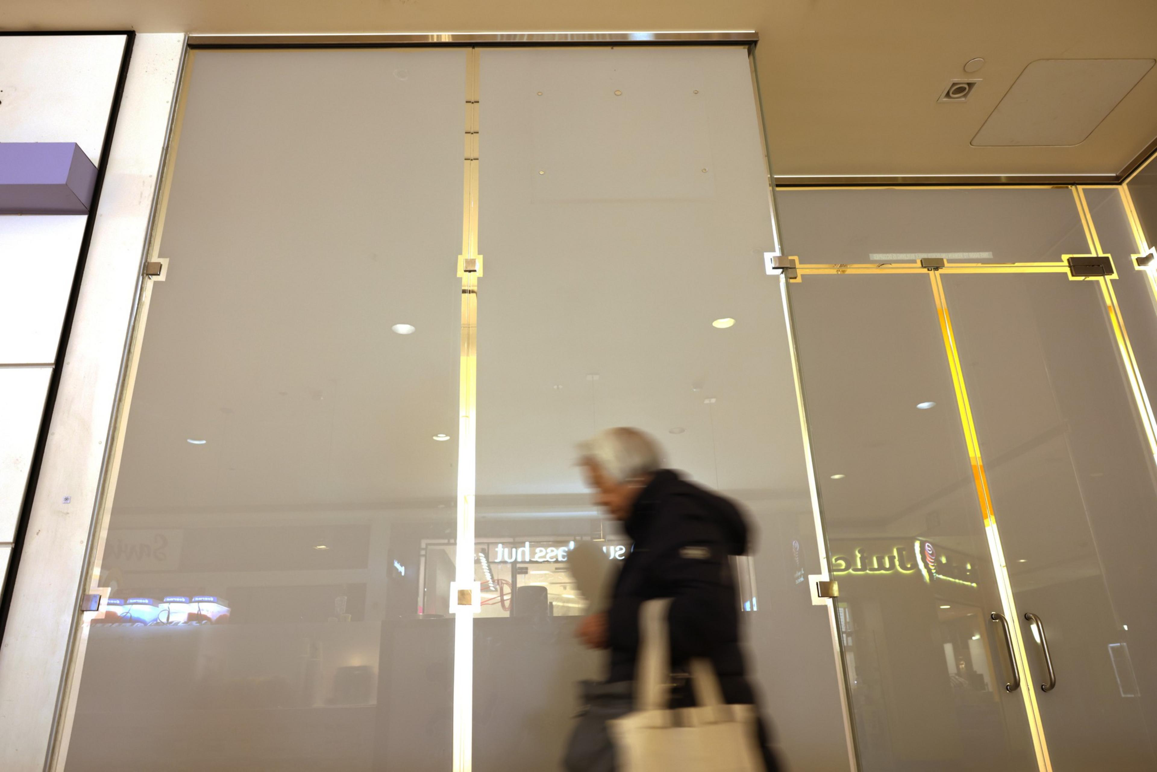 A blurred person walking past glass doors with reflections and light streaks.