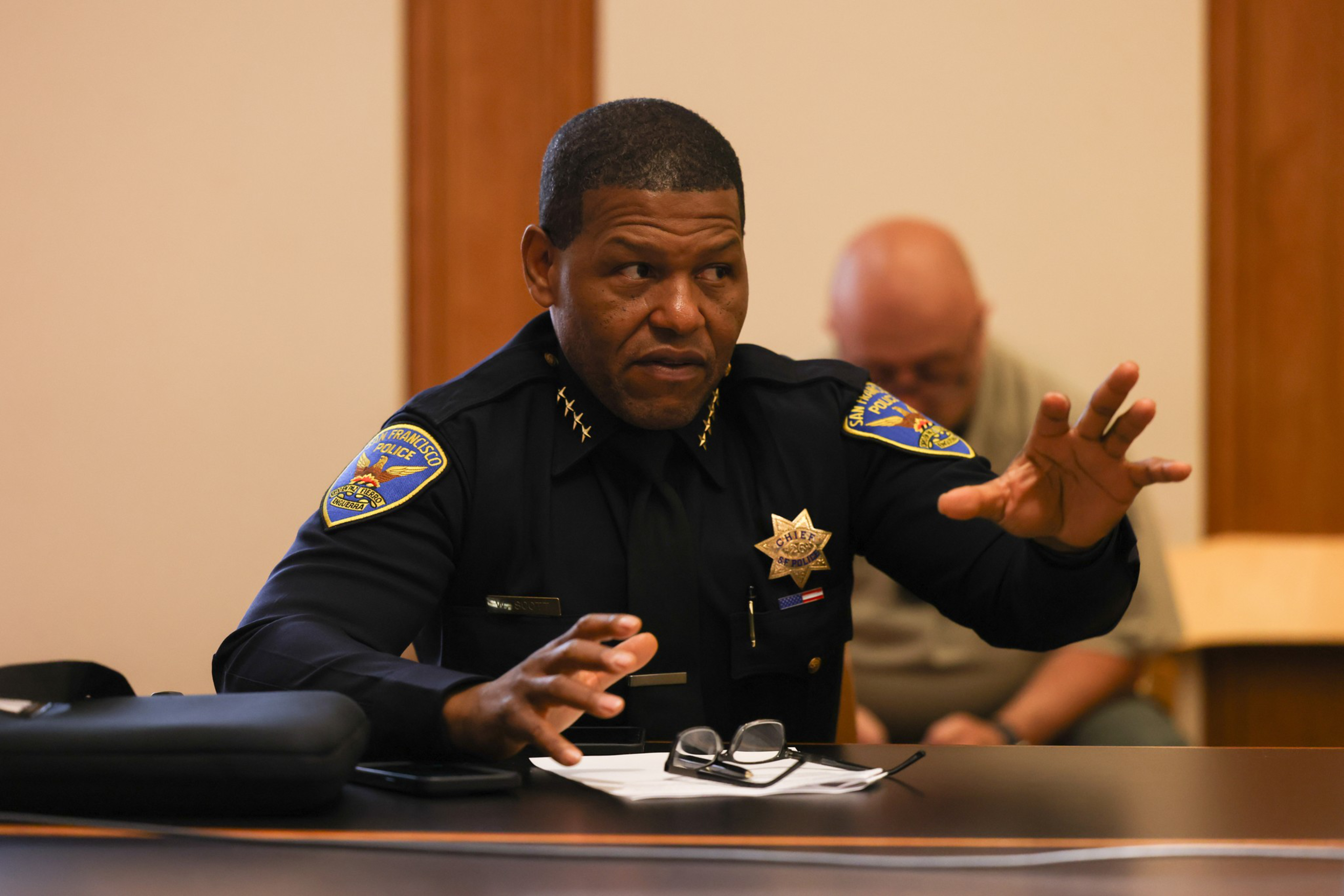 Police Chief Bill Scott, wearing his uniform, sits at a table speaking.