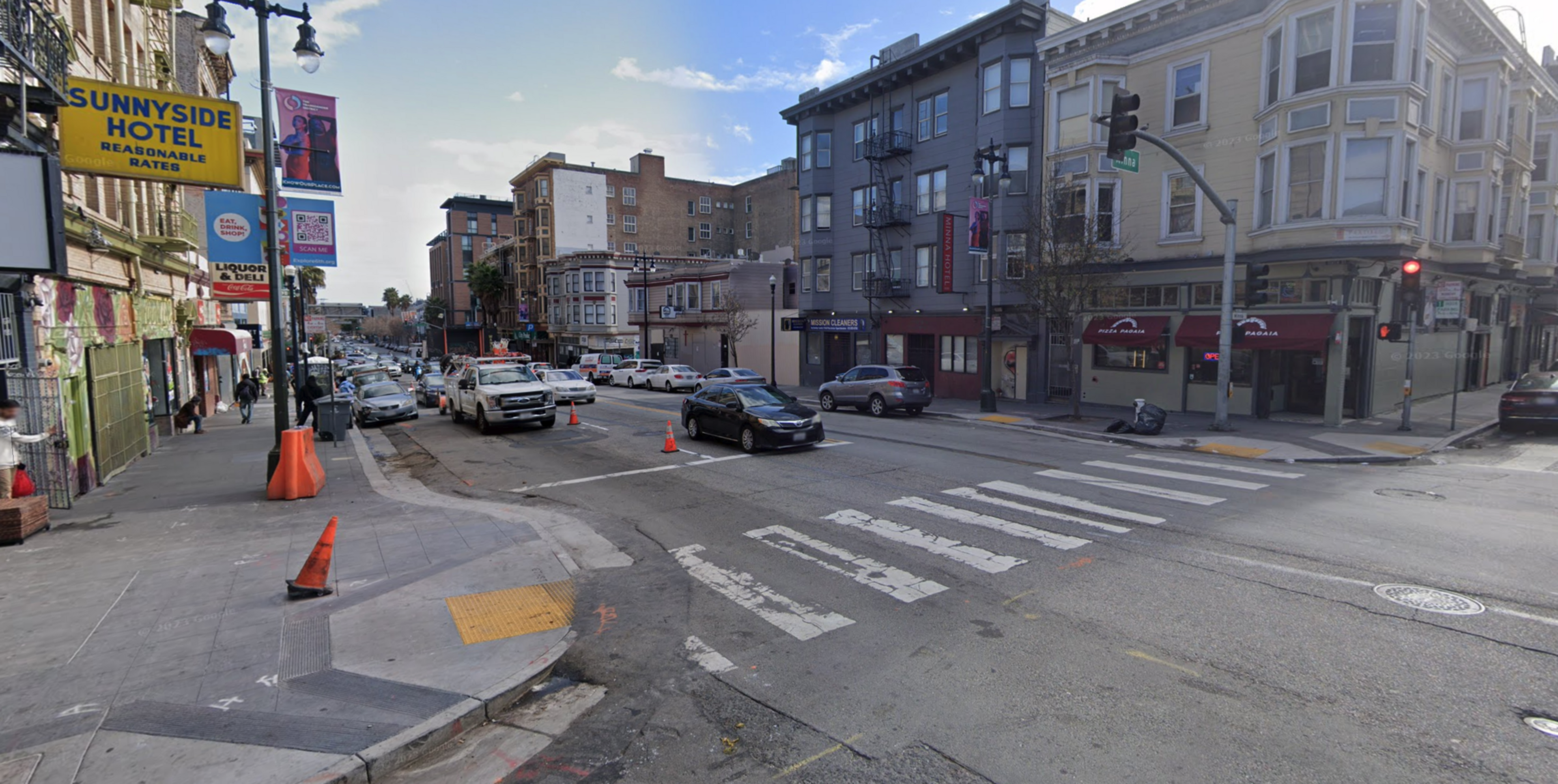 A city intersection with cars waiting at a red light, a sign for Sunnyside Hotel on the left, and multi-story buildings lining the streets.