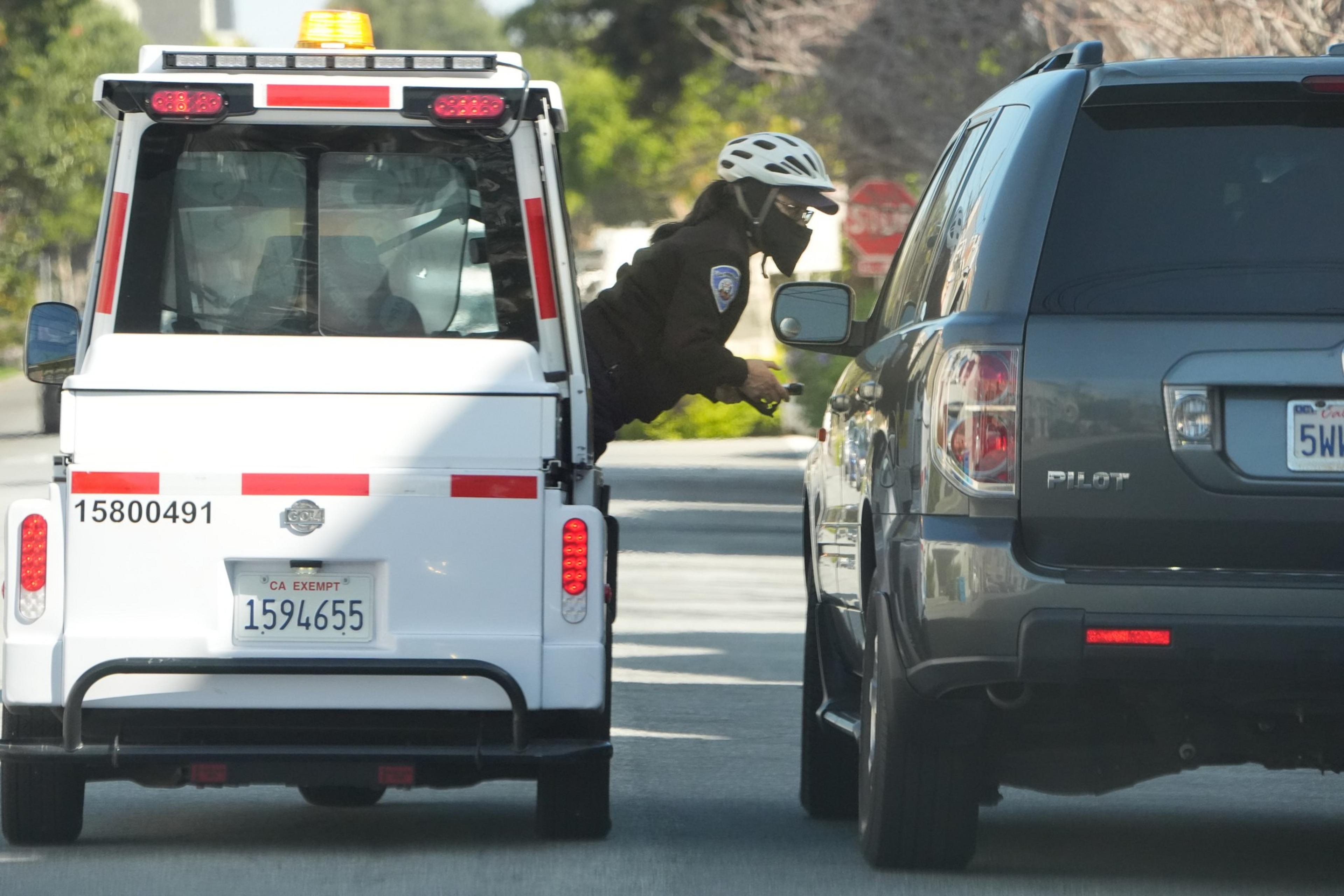 A police officer on a bike is speaking to a driver in a black SUV; a white service vehicle is nearby.